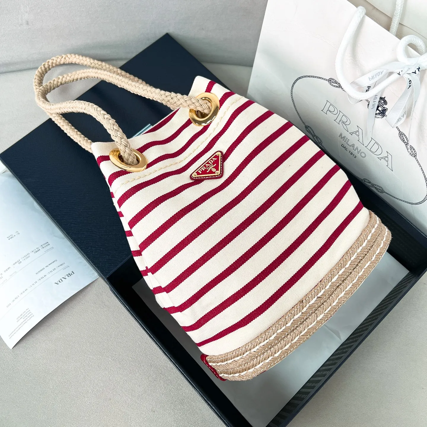 💰1160✨New product debut✨SS25 show new product Mariner canvas bucket bag 1BE082 Made of imported linen canvas fabric Nautical striped pattern Straw woven bottom highlights summer vacation style Sliding rope handle with classic golden triangle logo Drawstring buckle design Can adjust the space at will Lightweight can be packed and easy to match The randomness of different carrying methods and the ease of putting it anywhere Just pick it up and instantly transform into a pretty girl 🤩 Size: 28/23.5/16.5