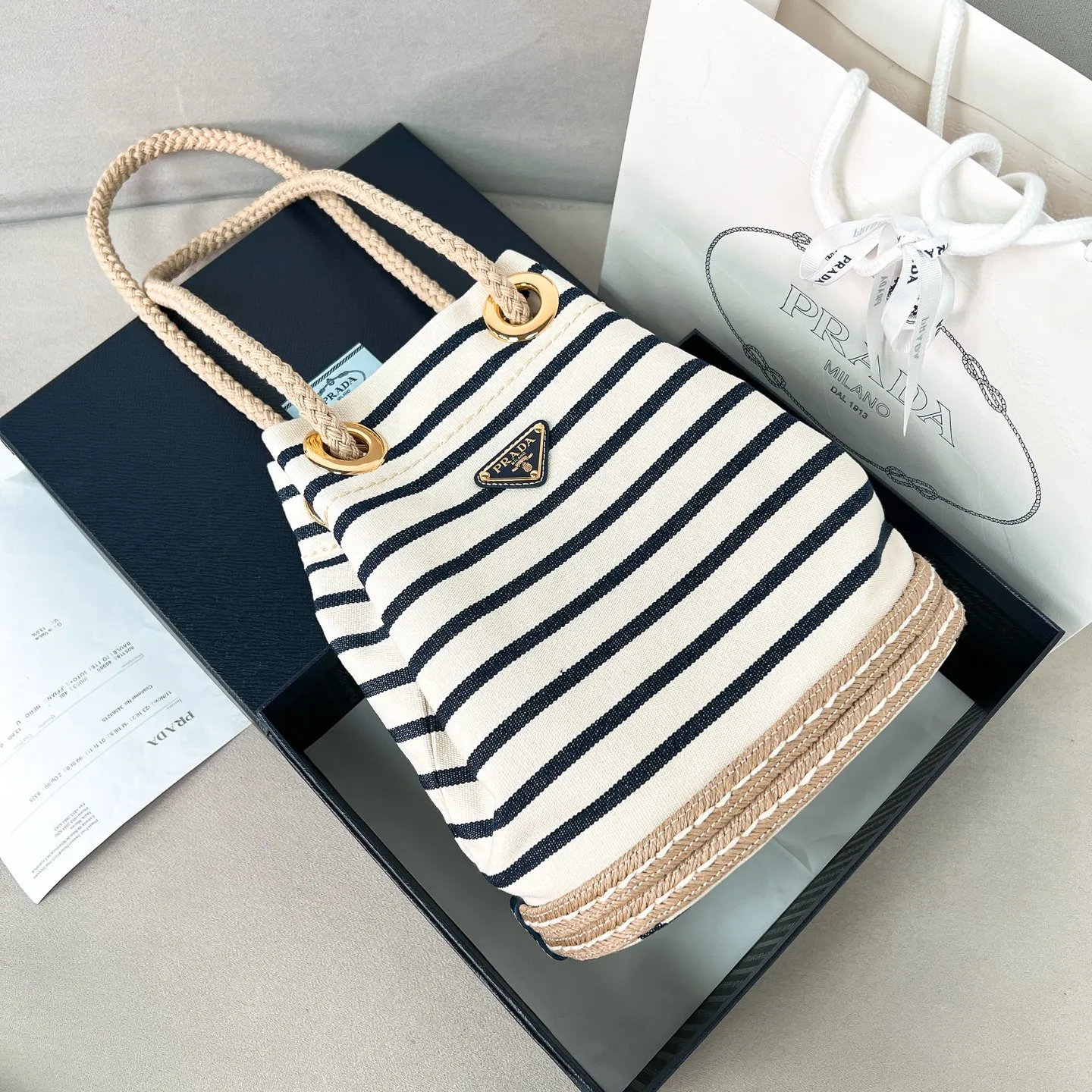 💰1160✨New product debut✨SS25 show new product Mariner canvas bucket bag 1BE082 Made of imported linen canvas fabric Nautical striped pattern Straw woven bottom highlights summer vacation style Sliding rope handle with classic golden triangle logo Drawstring buckle design Can adjust the space at will Lightweight can be packed and easy to match The randomness of different carrying methods and the ease of putting it anywhere Just pick it up and instantly transform into a pretty girl 🤩 Size: 28/23.5/16.5