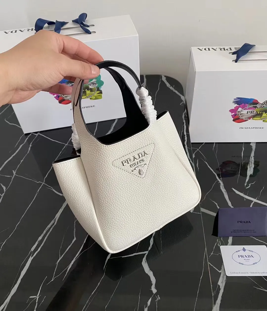 P1100¥ [Top original order] The latest 2022 vegetable basket tote bag mini model 1BA349 has arrived🎉🎉Soft and delicate pebbled calfskin tote bag, full leather inside and outside, equipped with double handles, decorated with silver metal logo, the overall body of the bag is very soft Lightweight, elegant and outstanding. The two side pockets not only meet the needs of exquisite storage but also add an elegant charm. It can be carried as a handbag or an armpit bag. It is a must-have handbag for fairies that perfectly combines classic heritage with the trend of the times. Size: 18︸15.5︸10CM!