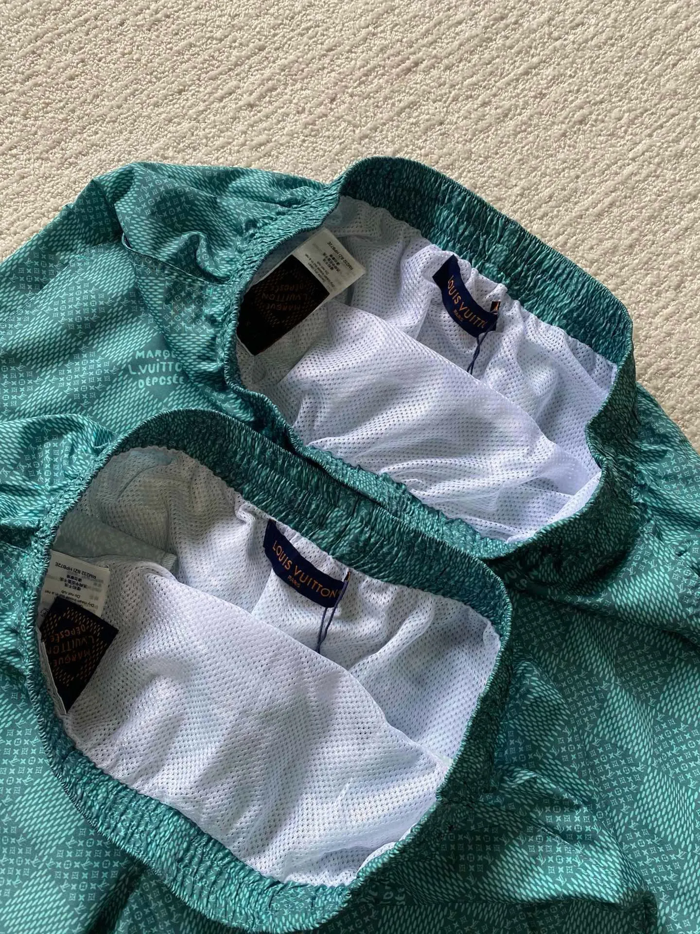 LU green checkerboard beach shorts ⚠️Original purchase, 700, polyester fiber fabric, imported digital printing, cut-piece printing design, standard fit, full-width Damier Monogram printing, drawstring elastic waist #Polyester fiber gray fabric Polyester fiber fabric has excellent wrinkle resistance and shape retention, which allows the shorts to maintain a good appearance after wearing and washing. At the same time, its high strength and good elastic recovery ability ensure the durability of the shorts.  The fabric is very thin and lighter than cotton fiber, so it is very comfortable to wear without feeling tight or compressive. It also has good softness and smooth touch, which increases the wearing comfort.  #Full-width Damier Monogram printing After the entire pattern is processed by image software, the computer control system sprays the printing ink directly onto the fabric through the nozzle of the inkjet printer as required to form the pattern. It is a precise printing controlled by a computer. The digital image is extremely precise. After the digital image is formed, the image is adjusted and printed. After adjusting the image, inkjet printing is performed on a digital printing machine. The ink is directly printed on the surface of the fabric, and the fabric surface penetrates to restore the quality of the original double-sided printing.  #Cut and sew the pattern to restore the original pattern effect. The pattern design is divided into multiple pieces and spliced ​​together, and it also changes due to size changes; even if it is the original version, the splices cannot be perfectly connected. Pieces can only be cut on the same horizontal line, and the patterns on the left and right trouser legs, and the front and rear panels of the entire piece should be arranged on the same horizontal line as much as possible, so that the sewing effect is consistent.  #straight sports shorts version. Fully elastic high waist with adjustable waist size. The front end of the elastic waist rope has an engraved hardware clock. The inner elastic band at the waist is fixed to the outer material through multiple routings, so the elastic band will not flip over even when worn or washed. The zipper pockets are designed with diagonal inserts on both sides; both ends of the pocket are specially machine-knotted, making it strong, durable and washable.