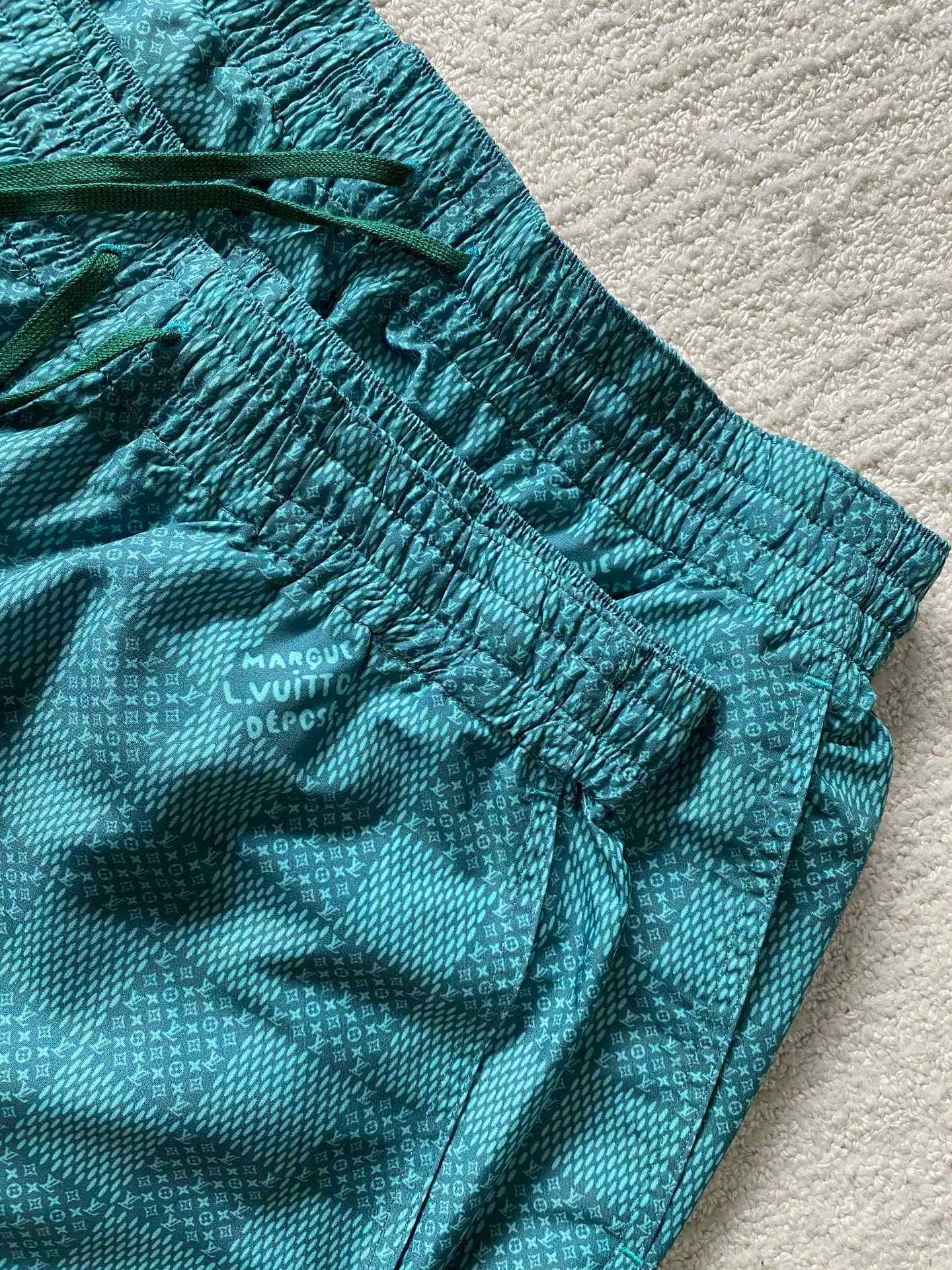LU green checkerboard beach shorts ⚠️Original purchase, 700, polyester fiber fabric, imported digital printing, cut-piece printing design, standard fit, full-width Damier Monogram printing, drawstring elastic waist #Polyester fiber gray fabric Polyester fiber fabric has excellent wrinkle resistance and shape retention, which allows the shorts to maintain a good appearance after wearing and washing. At the same time, its high strength and good elastic recovery ability ensure the durability of the shorts.  The fabric is very thin and lighter than cotton fiber, so it is very comfortable to wear without feeling tight or compressive. It also has good softness and smooth touch, which increases the wearing comfort.  #Full-width Damier Monogram printing After the entire pattern is processed by image software, the computer control system sprays the printing ink directly onto the fabric through the nozzle of the inkjet printer as required to form the pattern. It is a precise printing controlled by a computer. The digital image is extremely precise. After the digital image is formed, the image is adjusted and printed. After adjusting the image, inkjet printing is performed on a digital printing machine. The ink is directly printed on the surface of the fabric, and the fabric surface penetrates to restore the quality of the original double-sided printing.  #Cut and sew the pattern to restore the original pattern effect. The pattern design is divided into multiple pieces and spliced ​​together, and it also changes due to size changes; even if it is the original version, the splices cannot be perfectly connected. Pieces can only be cut on the same horizontal line, and the patterns on the left and right trouser legs, and the front and rear panels of the entire piece should be arranged on the same horizontal line as much as possible, so that the sewing effect is consistent.  #straight sports shorts version. Fully elastic high waist with adjustable waist size. The front end of the elastic waist rope has an engraved hardware clock. The inner elastic band at the waist is fixed to the outer material through multiple routings, so the elastic band will not flip over even when worn or washed. The zipper pockets are designed with diagonal inserts on both sides; both ends of the pocket are specially machine-knotted, making it strong, durable and washable.