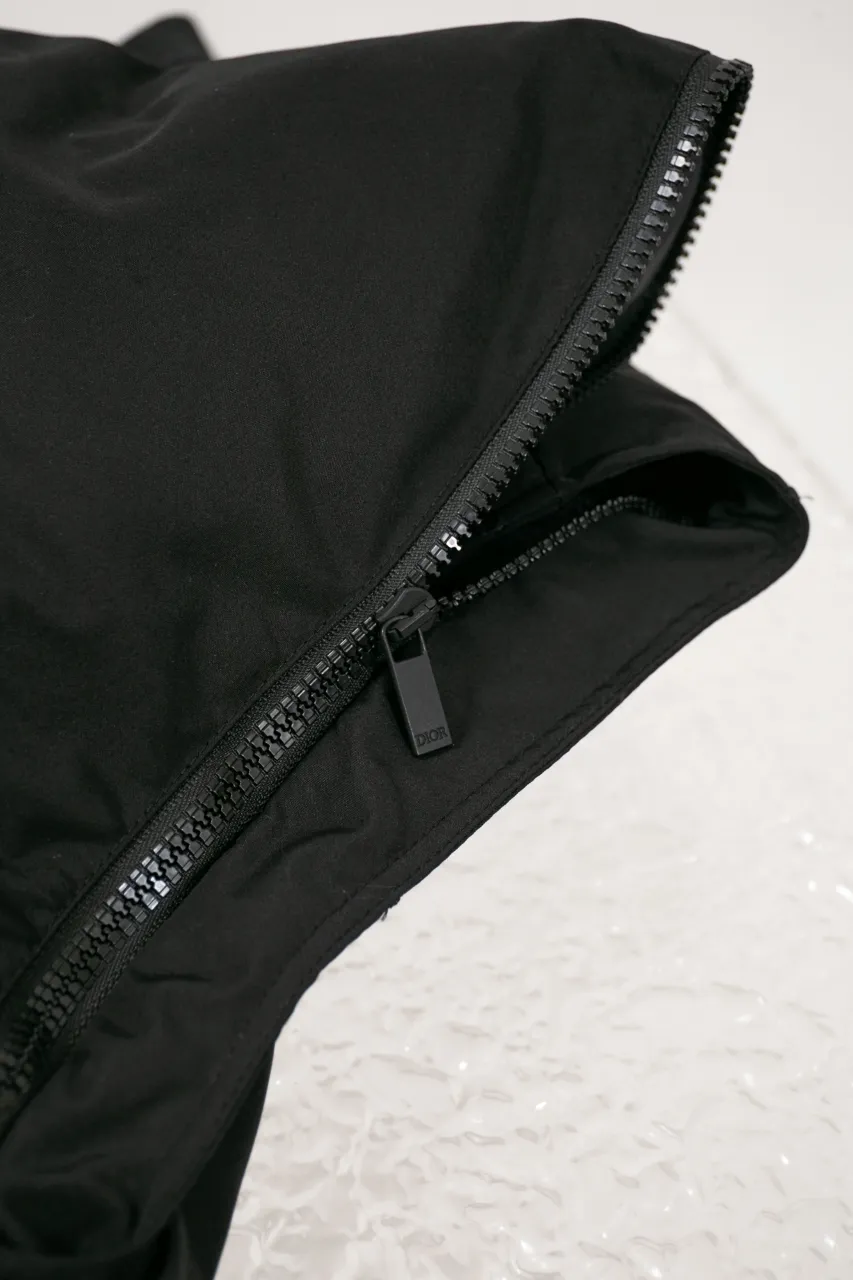 DIOR AND LEWIS HAMILTON JACKET Black technical fabric with removable sleeves This jacket is from the DIOR AND LEWIS HAMILTON limited series. Crafted from black technical fabric and embellished with DIOR AND LEWIS HAMILTON embroidery, the graphic design highlights the iconic Dior signature. With detachable sleeves, it can be worn in two different ways. It can be paired with jeans to create a low-key sporty look. DIOR AND LEWIS HAMILTON Embroidery and zip Knitted collar Detachable sleeves Front and internal flapless pockets Body: 100% nylon, Lining: 100% nylon