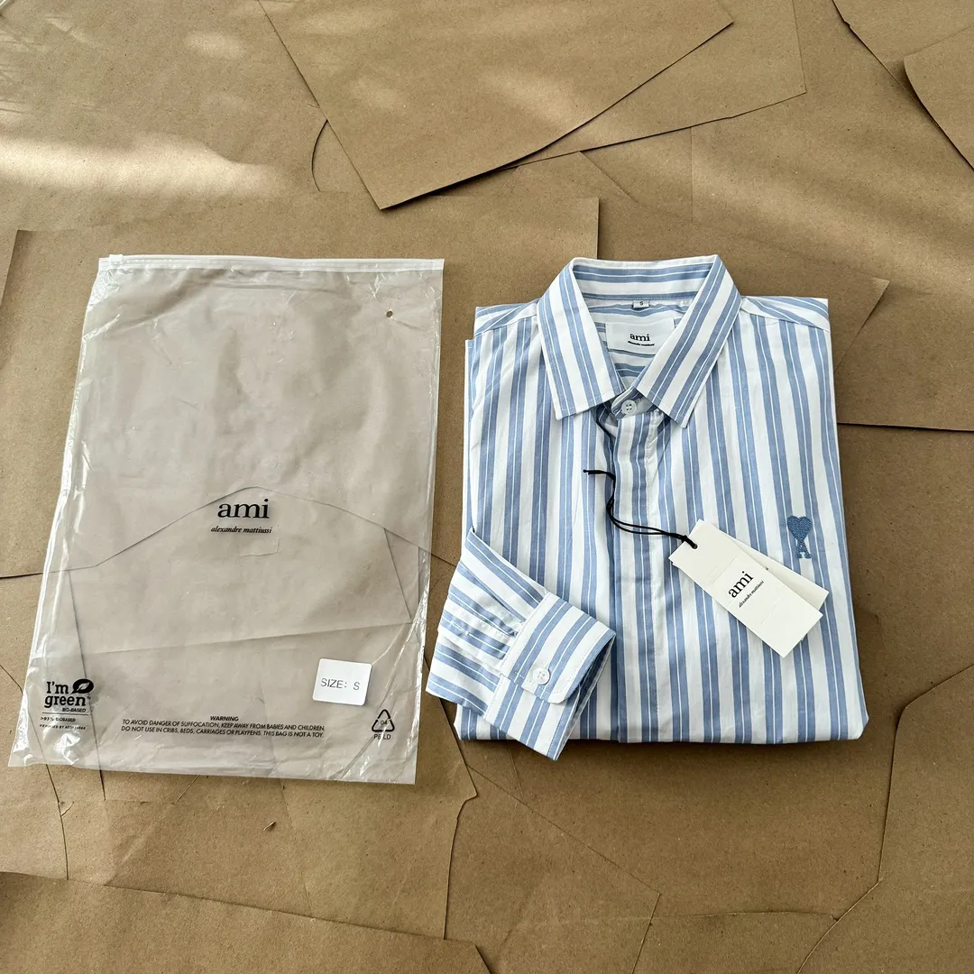 Ami Paris Oxford cotton button-down corner collar casual shirt-blue heart thick striped long-sleeved shirt-same style for men and women. Blue small love letter embroidery decoration fashionable and versatile long-sleeved shirt! On sale simultaneously at counters!  A well-known French affordable luxury fashion brand. The brand's classic elements are embellishments sought after by major celebrities. Its basic simple design and fashionable style make it a must-have couple's shirt for men and women!  Made of custom-woven 100% Oxford cloth pure cotton, it feels soft and delicate, has excellent moisture absorption and perspiration performance, and is very comfortable and skin-friendly when worn next to the skin! The chest of the shirt is decorated with the classic love letter A logo embroidery. The top-notch embroidery technology is tight, full and full of details, and is cleverly embellished with bright red. It carries all the eye-catching points. It follows the consistent minimalist French attitude. The fabric is soft and comfortable, suitable for any versatile casual shirt couple!  Color: Blue Stripe Size: S-XL S: Bust 106 Shoulder Width 47 Clothing Length 71 Sleeve Length 60 M: Bust 110 Shoulder Width 48 Clothing Length 73 Sleeve Length 61 L: Bust 114 Shoulder Width 49 Clothing Length 75 Sleeve Length 62