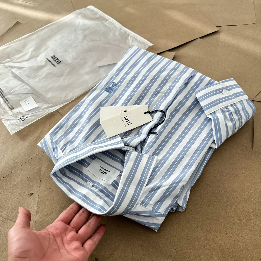Ami Paris Oxford cotton button-down corner collar casual shirt-blue heart thick striped long-sleeved shirt-same style for men and women. Blue small love letter embroidery decoration fashionable and versatile long-sleeved shirt! On sale simultaneously at counters!  A well-known French affordable luxury fashion brand. The brand's classic elements are embellishments sought after by major celebrities. Its basic simple design and fashionable style make it a must-have couple's shirt for men and women!  Made of custom-woven 100% Oxford cloth pure cotton, it feels soft and delicate, has excellent moisture absorption and perspiration performance, and is very comfortable and skin-friendly when worn next to the skin! The chest of the shirt is decorated with the classic love letter A logo embroidery. The top-notch embroidery technology is tight, full and full of details, and is cleverly embellished with bright red. It carries all the eye-catching points. It follows the consistent minimalist French attitude. The fabric is soft and comfortable, suitable for any versatile casual shirt couple!  Color: Blue Stripe Size: S-XL S: Bust 106 Shoulder Width 47 Clothing Length 71 Sleeve Length 60 M: Bust 110 Shoulder Width 48 Clothing Length 73 Sleeve Length 61 L: Bust 114 Shoulder Width 49 Clothing Length 75 Sleeve Length 62