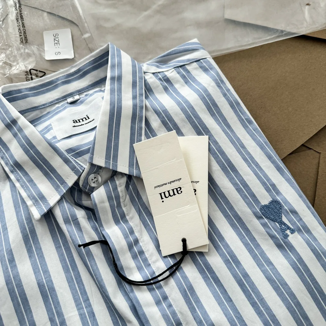 Ami Paris Oxford cotton button-down corner collar casual shirt-blue heart thick striped long-sleeved shirt-same style for men and women. Blue small love letter embroidery decoration fashionable and versatile long-sleeved shirt! On sale simultaneously at counters!  A well-known French affordable luxury fashion brand. The brand's classic elements are embellishments sought after by major celebrities. Its basic simple design and fashionable style make it a must-have couple's shirt for men and women!  Made of custom-woven 100% Oxford cloth pure cotton, it feels soft and delicate, has excellent moisture absorption and perspiration performance, and is very comfortable and skin-friendly when worn next to the skin! The chest of the shirt is decorated with the classic love letter A logo embroidery. The top-notch embroidery technology is tight, full and full of details, and is cleverly embellished with bright red. It carries all the eye-catching points. It follows the consistent minimalist French attitude. The fabric is soft and comfortable, suitable for any versatile casual shirt couple!  Color: Blue Stripe Size: S-XL S: Bust 106 Shoulder Width 47 Clothing Length 71 Sleeve Length 60 M: Bust 110 Shoulder Width 48 Clothing Length 73 Sleeve Length 61 L: Bust 114 Shoulder Width 49 Clothing Length 75 Sleeve Length 62