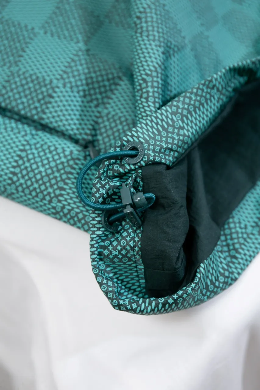 LV Printed Nylon Hooded Windproof Jacket This technical hooded windbreaker combines functional details with the season's nautical theme, sublimating the trend with an all-over Damier Monogram pattern, incorporating micro Monogram details and the Marque L.Vuitton Déposée logo. Fresh colors complete the casual design.  SMLXL