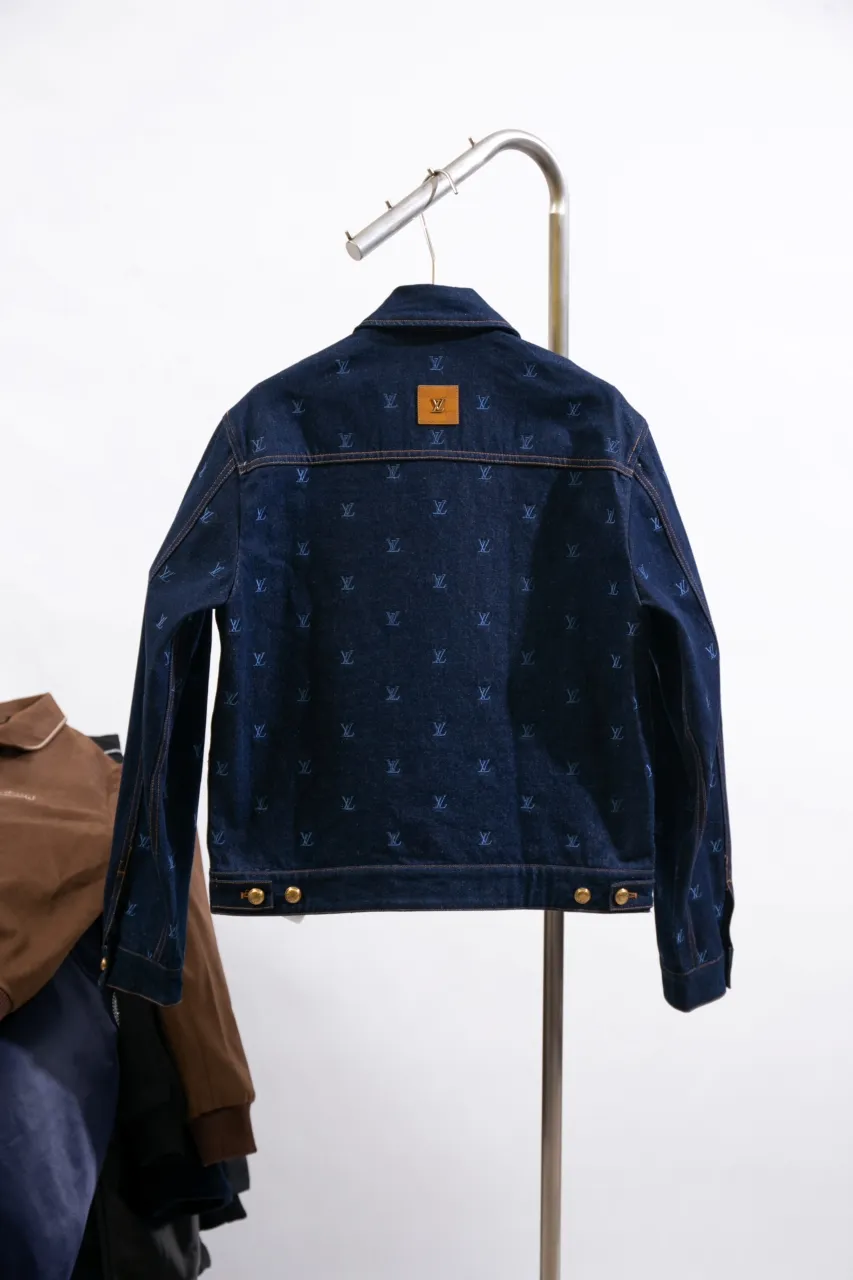 LV Embroidered Denim Tunic Jacket This belted jacket is crafted from washed denim in a classic trucker jacket silhouette, with yarn embroidery depicting the all-over LV Blason pattern and contrasting topstitching and button details. Metallic LV accents and a Damier nubuck label perch on the back make it perfect for the season with the matching trousers.  Regular fit All-over LV Blason embroidery Rear nubuck label with metallic LV accents Denim buttons at front