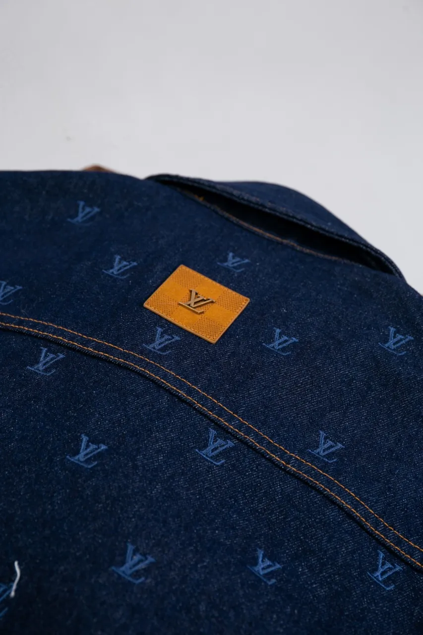 LV Embroidered Denim Tunic Jacket This belted jacket is crafted from washed denim in a classic trucker jacket silhouette, with yarn embroidery depicting the all-over LV Blason pattern and contrasting topstitching and button details. Metallic LV accents and a Damier nubuck label perch on the back make it perfect for the season with the matching trousers.  Regular fit All-over LV Blason embroidery Rear nubuck label with metallic LV accents Denim buttons at front