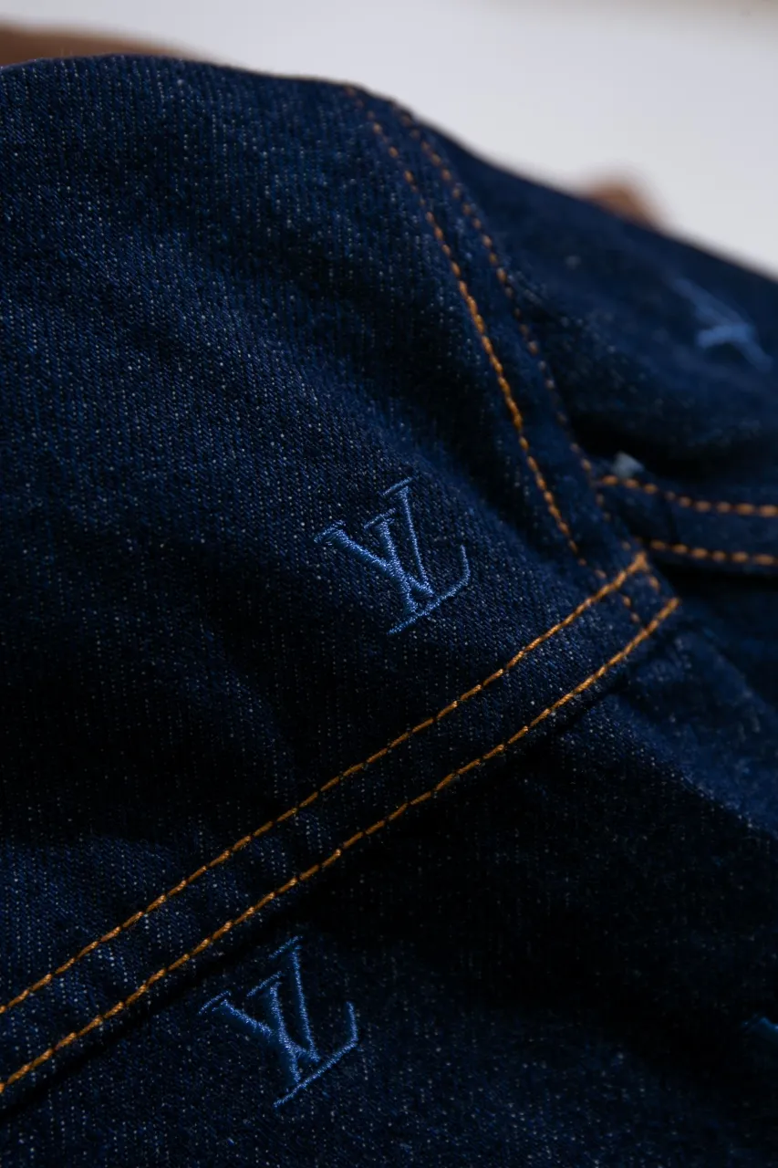 LV Embroidered Denim Tunic Jacket This belted jacket is crafted from washed denim in a classic trucker jacket silhouette, with yarn embroidery depicting the all-over LV Blason pattern and contrasting topstitching and button details. Metallic LV accents and a Damier nubuck label perch on the back make it perfect for the season with the matching trousers.  Regular fit All-over LV Blason embroidery Rear nubuck label with metallic LV accents Denim buttons at front