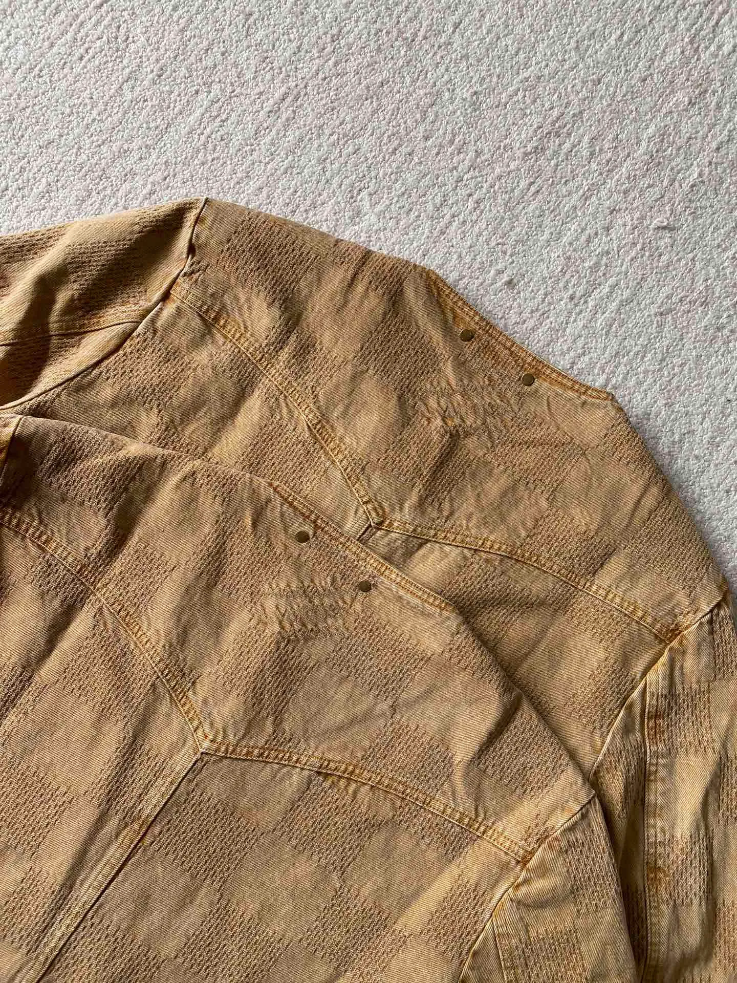 LV saddle checkerboard denim suit • Jacket ⚠️Original purchase, 000; standard fit, checkerboard element jacquard, lower left pocket embellished with Saddle patch, collarless curved hem, front patch pockets including chest pockets, hand-stitched button details, new button series buttons exclusively developed #logo integrated into 3D Damier jacquard 3D Damier jacquard denim fabric is an innovative fabric that combines jacquard technology and the characteristics of denim. The classic plaid pattern is combined with 3D jacquard technology to weave three-dimensional patterns on the fabric through a loom.  The fabric presents an exquisite plaid pattern in appearance, and the pattern is made three-dimensional and layered through jacquard technology. At the same time, it retains the original tough, wear-resistant and durable properties of denim, making the clothes more durable.  #Grey cloth retro coloring process is a process that uses a specific process to make the originally white denim show a retro, worn-out special color effect. Clean the white denim fabric to remove surface impurities and residues. Through specific processing methods, the fabric can maintain stable dimensions during subsequent processing.  Choose the appropriate natural dye for the desired distressing effect on the plate. The dye is evenly applied to the fabric, giving it a gradient coloring effect. After dyeing is completed, necessary cleaning and color fixing treatments are required to ensure color stability and durability.  # Sandwashed, Faded and Distressed Effect Sandwashed, faded and distressed denim fabric is a specially treated denim fabric that exhibits a whitened and distressed effect. This fabric uses a sand-washing process and special dyeing technology to create a natural wear and fading effect on the denim after washing, making it look more vintage and historical.  # Collarless curved hem shirt version Collarless curved hem denim shirt version is a unique and fashionable clothing design. The entire shirt style looks simpler and lighter. There is no traditional collar, focusing more on comfort and freedom; the curved hem fits the body curve better. Balance the visual effect of the entire shirt and make it look more harmonious and unified.  Opposite patch pocket design; door sills are opened and closed with new hand-stitched phantom sapphire buttons; cuffs are decorated with matching embellishments; a full set of molded custom hardware with clear and delicate gem surface engravings and environmentally friendly plating; basic accessories are fully equipped.