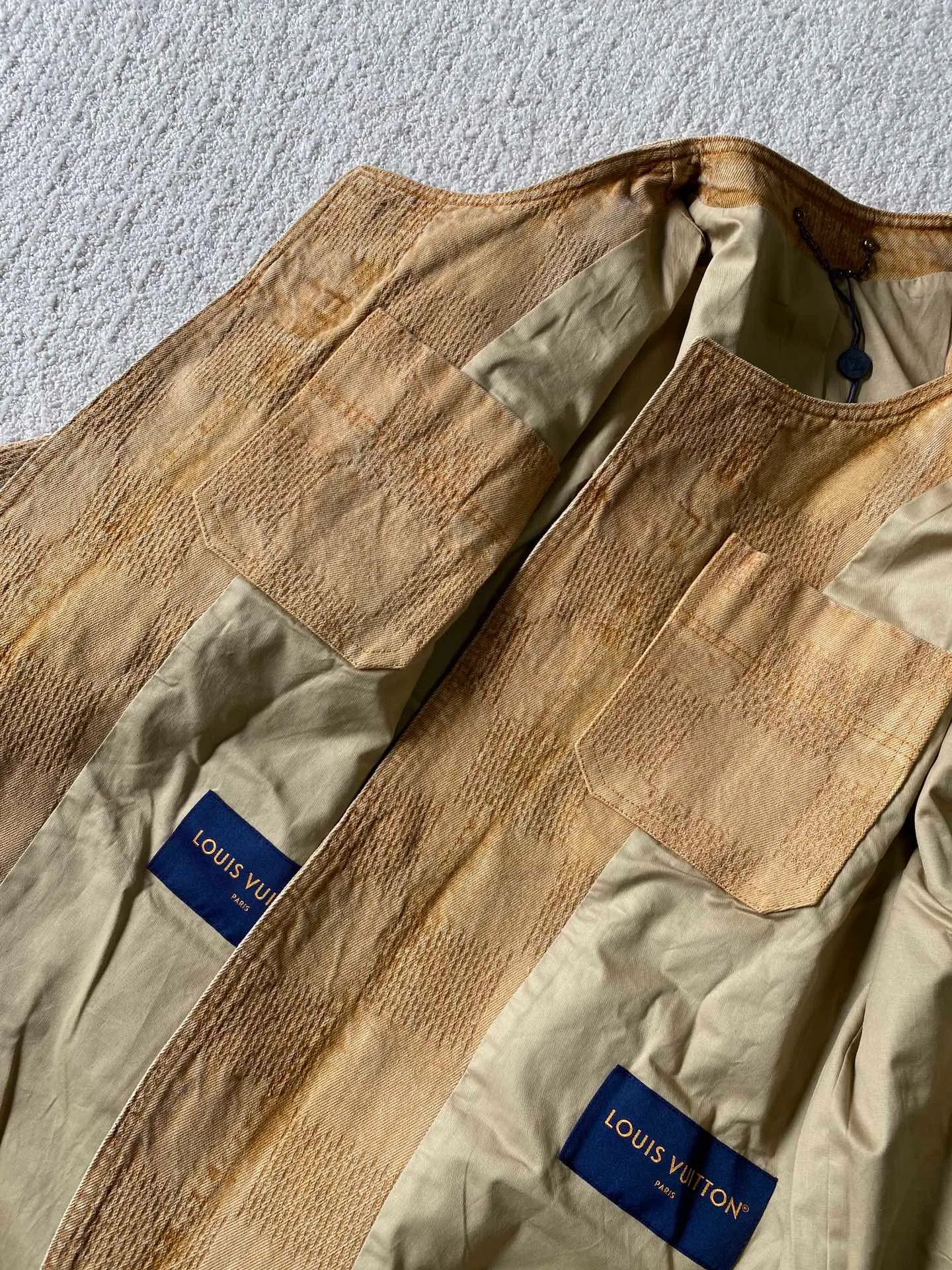 LV saddle checkerboard denim suit • Jacket ⚠️Original purchase, 000; standard fit, checkerboard element jacquard, lower left pocket embellished with Saddle patch, collarless curved hem, front patch pockets including chest pockets, hand-stitched button details, new button series buttons exclusively developed #logo integrated into 3D Damier jacquard 3D Damier jacquard denim fabric is an innovative fabric that combines jacquard technology and the characteristics of denim. The classic plaid pattern is combined with 3D jacquard technology to weave three-dimensional patterns on the fabric through a loom.  The fabric presents an exquisite plaid pattern in appearance, and the pattern is made three-dimensional and layered through jacquard technology. At the same time, it retains the original tough, wear-resistant and durable properties of denim, making the clothes more durable.  #Grey cloth retro coloring process is a process that uses a specific process to make the originally white denim show a retro, worn-out special color effect. Clean the white denim fabric to remove surface impurities and residues. Through specific processing methods, the fabric can maintain stable dimensions during subsequent processing.  Choose the appropriate natural dye for the desired distressing effect on the plate. The dye is evenly applied to the fabric, giving it a gradient coloring effect. After dyeing is completed, necessary cleaning and color fixing treatments are required to ensure color stability and durability.  # Sandwashed, Faded and Distressed Effect Sandwashed, faded and distressed denim fabric is a specially treated denim fabric that exhibits a whitened and distressed effect. This fabric uses a sand-washing process and special dyeing technology to create a natural wear and fading effect on the denim after washing, making it look more vintage and historical.  # Collarless curved hem shirt version Collarless curved hem denim shirt version is a unique and fashionable clothing design. The entire shirt style looks simpler and lighter. There is no traditional collar, focusing more on comfort and freedom; the curved hem fits the body curve better. Balance the visual effect of the entire shirt and make it look more harmonious and unified.  Opposite patch pocket design; door sills are opened and closed with new hand-stitched phantom sapphire buttons; cuffs are decorated with matching embellishments; a full set of molded custom hardware with clear and delicate gem surface engravings and environmentally friendly plating; basic accessories are fully equipped.