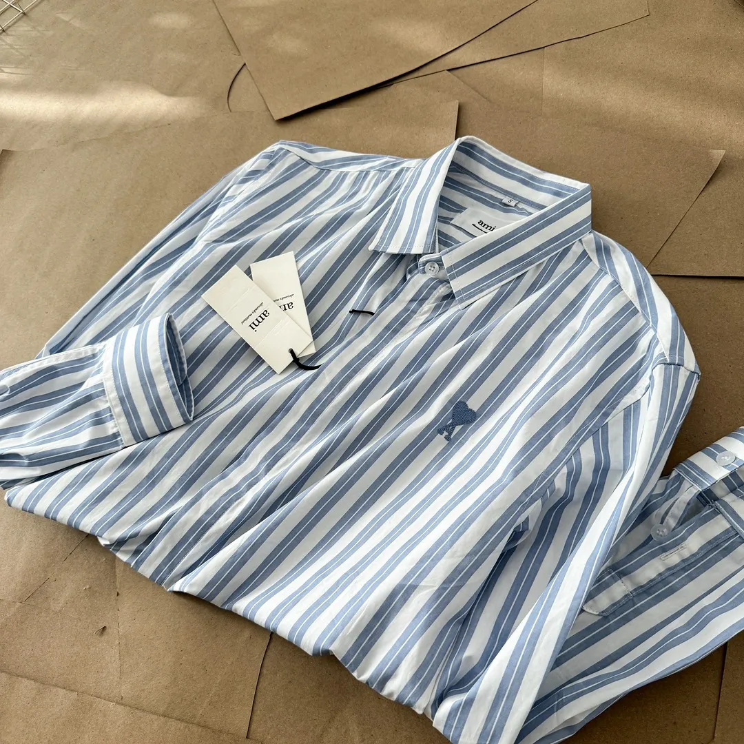 Ami Paris Oxford cotton button-down corner collar casual shirt-blue heart thick striped long-sleeved shirt-same style for men and women. Blue small love letter embroidery decoration fashionable and versatile long-sleeved shirt! On sale simultaneously at counters!  A well-known French affordable luxury fashion brand. The brand's classic elements are embellishments sought after by major celebrities. Its basic simple design and fashionable style make it a must-have couple's shirt for men and women!  Made of custom-woven 100% Oxford cloth pure cotton, it feels soft and delicate, has excellent moisture absorption and perspiration performance, and is very comfortable and skin-friendly when worn next to the skin! The chest of the shirt is decorated with the classic love letter A logo embroidery. The top-notch embroidery technology is tight, full and full of details, and is cleverly embellished with bright red. It carries all the eye-catching points. It follows the consistent minimalist French attitude. The fabric is soft and comfortable, suitable for any versatile casual shirt couple!  Color: Blue Stripe Size: S-XL S: Bust 106 Shoulder Width 47 Clothing Length 71 Sleeve Length 60 M: Bust 110 Shoulder Width 48 Clothing Length 73 Sleeve Length 61 L: Bust 114 Shoulder Width 49 Clothing Length 75 Sleeve Length 62