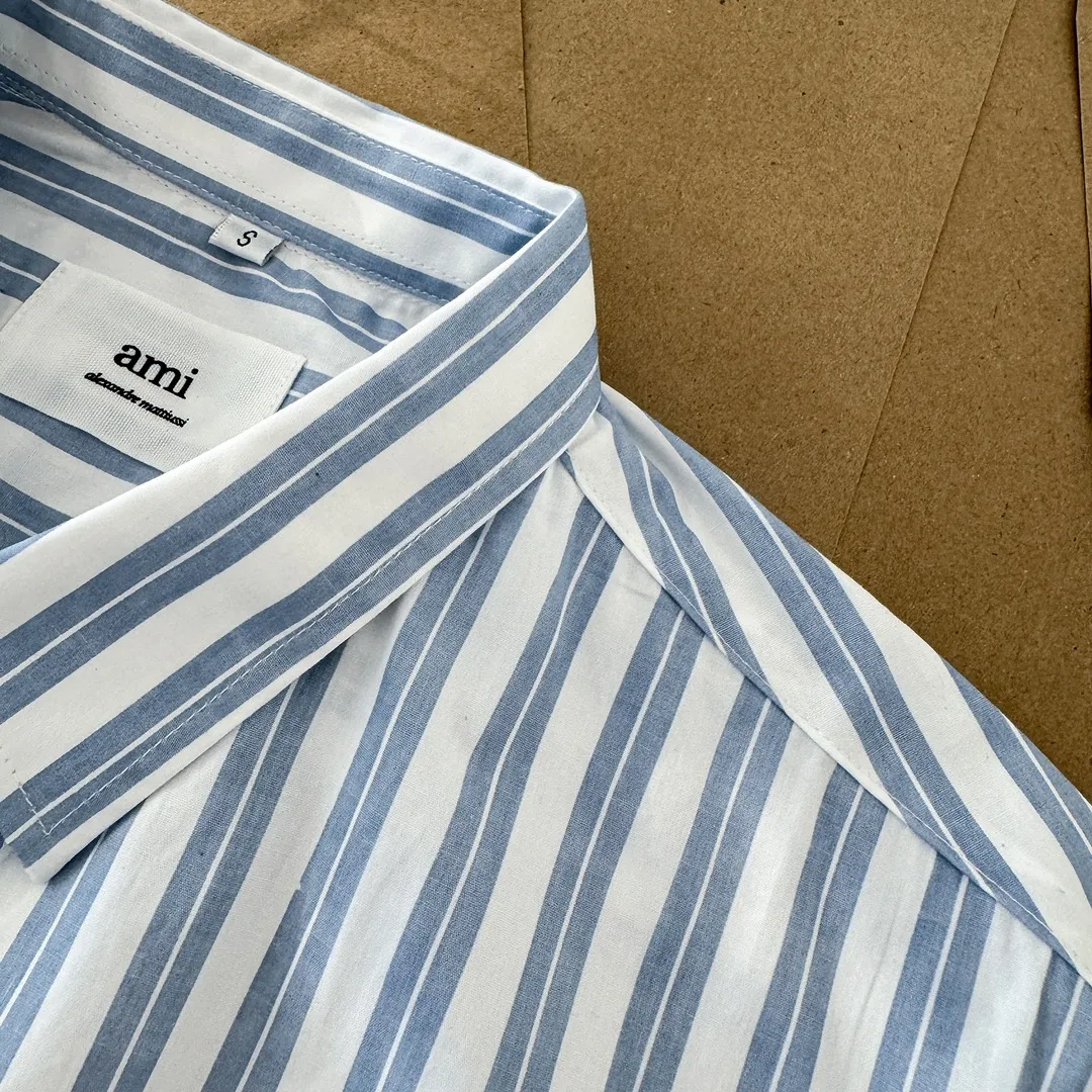 Ami Paris Oxford cotton button-down corner collar casual shirt-blue heart thick striped long-sleeved shirt-same style for men and women. Blue small love letter embroidery decoration fashionable and versatile long-sleeved shirt! On sale simultaneously at counters!  A well-known French affordable luxury fashion brand. The brand's classic elements are embellishments sought after by major celebrities. Its basic simple design and fashionable style make it a must-have couple's shirt for men and women!  Made of custom-woven 100% Oxford cloth pure cotton, it feels soft and delicate, has excellent moisture absorption and perspiration performance, and is very comfortable and skin-friendly when worn next to the skin! The chest of the shirt is decorated with the classic love letter A logo embroidery. The top-notch embroidery technology is tight, full and full of details, and is cleverly embellished with bright red. It carries all the eye-catching points. It follows the consistent minimalist French attitude. The fabric is soft and comfortable, suitable for any versatile casual shirt couple!  Color: Blue Stripe Size: S-XL S: Bust 106 Shoulder Width 47 Clothing Length 71 Sleeve Length 60 M: Bust 110 Shoulder Width 48 Clothing Length 73 Sleeve Length 61 L: Bust 114 Shoulder Width 49 Clothing Length 75 Sleeve Length 62