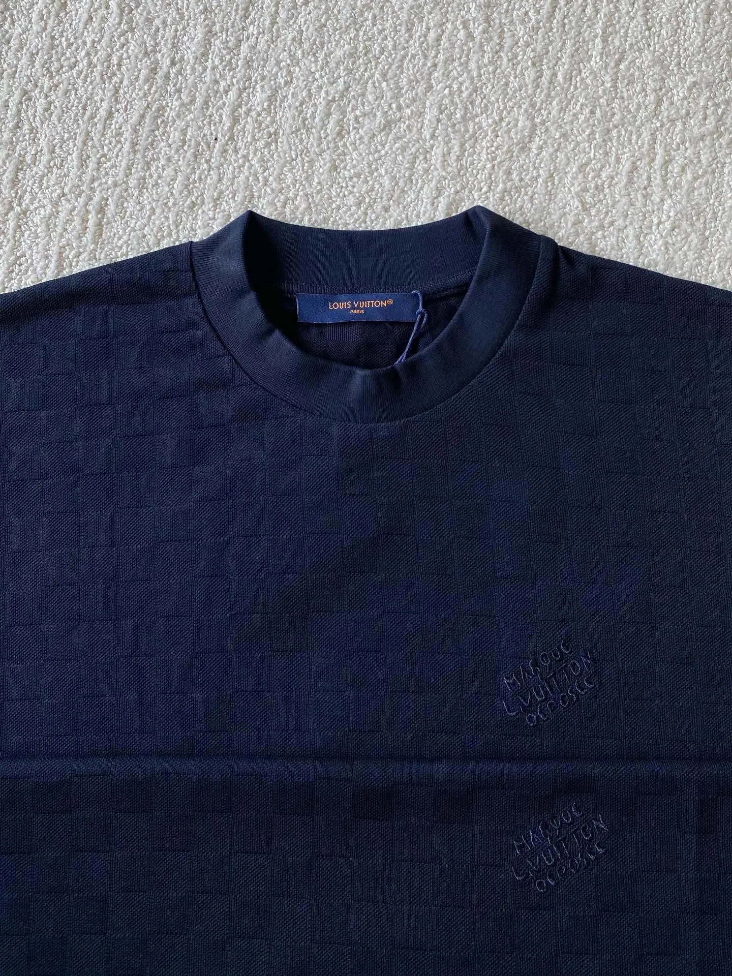 LU piqué round neck short sleeves. Available colors: navy blue, apricot white. ⚠️Original, 350 purchase; piqué jacquard fabric, standard version, full-width Damier jacquard piqué, chest Marque L.Uuitton déposée embroidery #full-width Damier jacquard piqué Navy blue · 32S double strand, 210g; apricot white · 80S double strand, 120g; with 32S double yarn thread, 320g. Pique jacquard fabric is a special fabric woven using a jacquard machine, with highly beautiful patterns and high-quality feel. This kind of fabric uses jacquard processing technology and uses various jacquard structures to make the yarns show a plaid pattern and form a bead-like finish on the surface of the fabric. The unique texture and visual effects of the fabric make it highly artistic.  #Chest Marque L Uuitton deposee embroidery The chest is embellished with simple letter patterns, and the letter size spacing effect is consistent. Using linen embroidery thread combined with encrypted processing, the embroidery body has a subtle matte visual texture; the embroidery effect is three-dimensional and full. The smaller the embroidery, the more sophisticated and demanding it is. The embroidery thread is made of imported material, which is more flexible and glossy than ordinary embroidery thread; the stitches are clear and smooth, and have a three-dimensional texture effect.  #Positioning Pattern Cutting and Sewing The whole piece positioning pattern sewing process is a fine and complex technology. During the cutting process, it is necessary to ensure that the pattern or texture of each piece can perfectly match other pieces. Through floral tailoring, the checkerboard pattern of ready-made garments appears neatly arranged.  #straight round neck version. Cut and sewed in floral position, standard H hanging version, with shoulder-length design. The vertical version emphasizes that the width of the shoulders, waist, and hem are basically the same, and it is simple and loose. The short sleeves are tailored to fit the body of the wearer. At the same time, the neckline, cuffs and hem of the short sleeves are all designed with double lines.