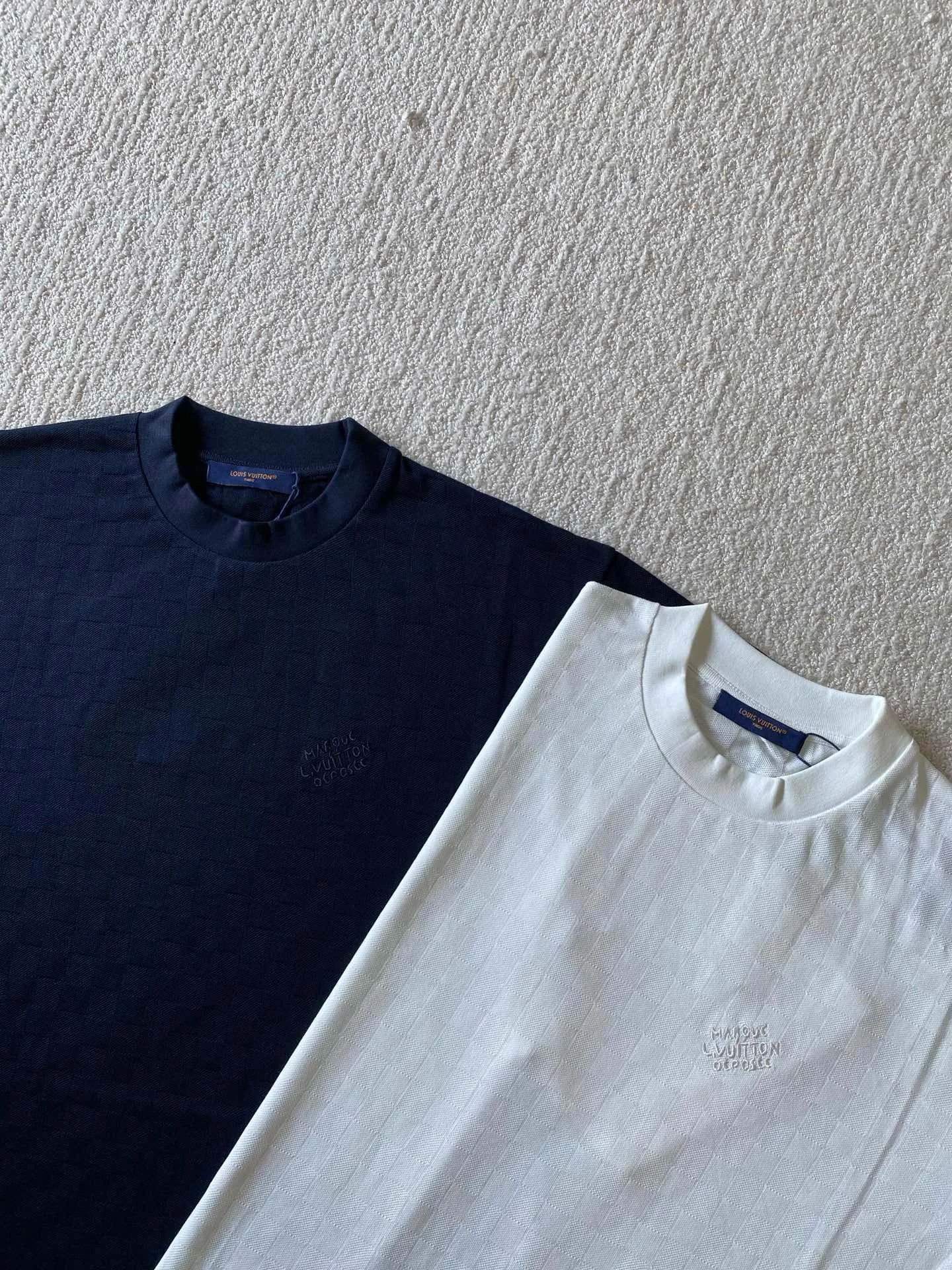 LU piqué round neck short sleeves. Available colors: navy blue, apricot white. ⚠️Original, 350 purchase; piqué jacquard fabric, standard version, full-width Damier jacquard piqué, chest Marque L.Uuitton déposée embroidery #full-width Damier jacquard piqué Navy blue · 32S double strand, 210g; apricot white · 80S double strand, 120g; with 32S double yarn thread, 320g. Pique jacquard fabric is a special fabric woven using a jacquard machine, with highly beautiful patterns and high-quality feel. This kind of fabric uses jacquard processing technology and uses various jacquard structures to make the yarns show a plaid pattern and form a bead-like finish on the surface of the fabric. The unique texture and visual effects of the fabric make it highly artistic.  #Chest Marque L Uuitton deposee embroidery The chest is embellished with simple letter patterns, and the letter size spacing effect is consistent. Using linen embroidery thread combined with encrypted processing, the embroidery body has a subtle matte visual texture; the embroidery effect is three-dimensional and full. The smaller the embroidery, the more sophisticated and demanding it is. The embroidery thread is made of imported material, which is more flexible and glossy than ordinary embroidery thread; the stitches are clear and smooth, and have a three-dimensional texture effect.  #Positioning Pattern Cutting and Sewing The whole piece positioning pattern sewing process is a fine and complex technology. During the cutting process, it is necessary to ensure that the pattern or texture of each piece can perfectly match other pieces. Through floral tailoring, the checkerboard pattern of ready-made garments appears neatly arranged.  #straight round neck version. Cut and sewed in floral position, standard H hanging version, with shoulder-length design. The vertical version emphasizes that the width of the shoulders, waist, and hem are basically the same, and it is simple and loose. The short sleeves are tailored to fit the body of the wearer. At the same time, the neckline, cuffs and hem of the short sleeves are all designed with double lines.