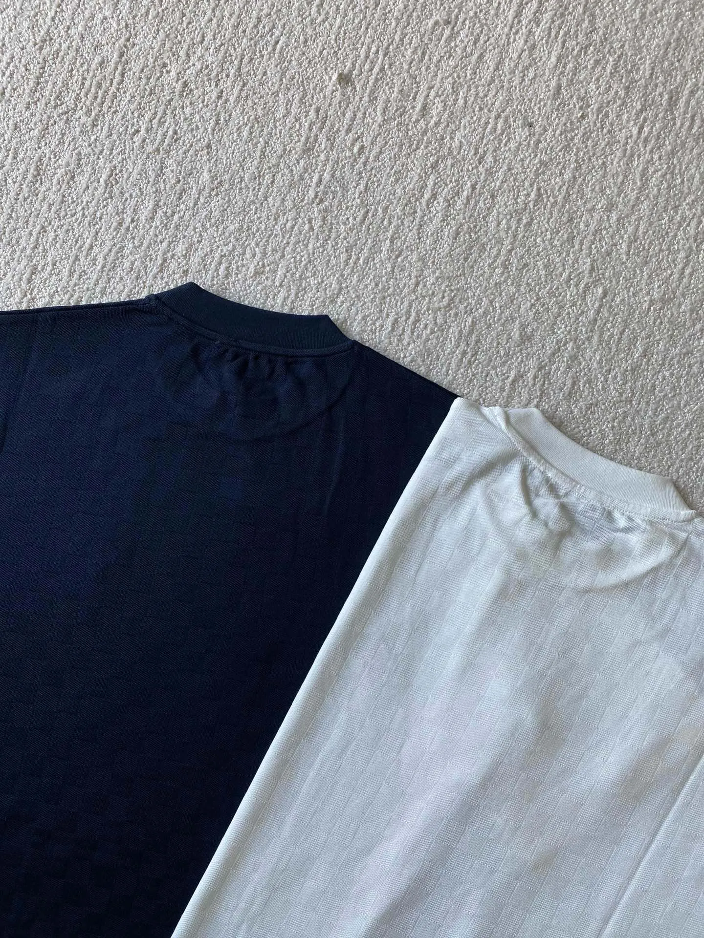 LU piqué round neck short sleeves. Available colors: navy blue, apricot white. ⚠️Original, 350 purchase; piqué jacquard fabric, standard version, full-width Damier jacquard piqué, chest Marque L.Uuitton déposée embroidery #full-width Damier jacquard piqué Navy blue · 32S double strand, 210g; apricot white · 80S double strand, 120g; with 32S double yarn thread, 320g. Pique jacquard fabric is a special fabric woven using a jacquard machine, with highly beautiful patterns and high-quality feel. This kind of fabric uses jacquard processing technology and uses various jacquard structures to make the yarns show a plaid pattern and form a bead-like finish on the surface of the fabric. The unique texture and visual effects of the fabric make it highly artistic.  #Chest Marque L Uuitton deposee embroidery The chest is embellished with simple letter patterns, and the letter size spacing effect is consistent. Using linen embroidery thread combined with encrypted processing, the embroidery body has a subtle matte visual texture; the embroidery effect is three-dimensional and full. The smaller the embroidery, the more sophisticated and demanding it is. The embroidery thread is made of imported material, which is more flexible and glossy than ordinary embroidery thread; the stitches are clear and smooth, and have a three-dimensional texture effect.  #Positioning Pattern Cutting and Sewing The whole piece positioning pattern sewing process is a fine and complex technology. During the cutting process, it is necessary to ensure that the pattern or texture of each piece can perfectly match other pieces. Through floral tailoring, the checkerboard pattern of ready-made garments appears neatly arranged.  #straight round neck version. Cut and sewed in floral position, standard H hanging version, with shoulder-length design. The vertical version emphasizes that the width of the shoulders, waist, and hem are basically the same, and it is simple and loose. The short sleeves are tailored to fit the body of the wearer. At the same time, the neckline, cuffs and hem of the short sleeves are all designed with double lines.
