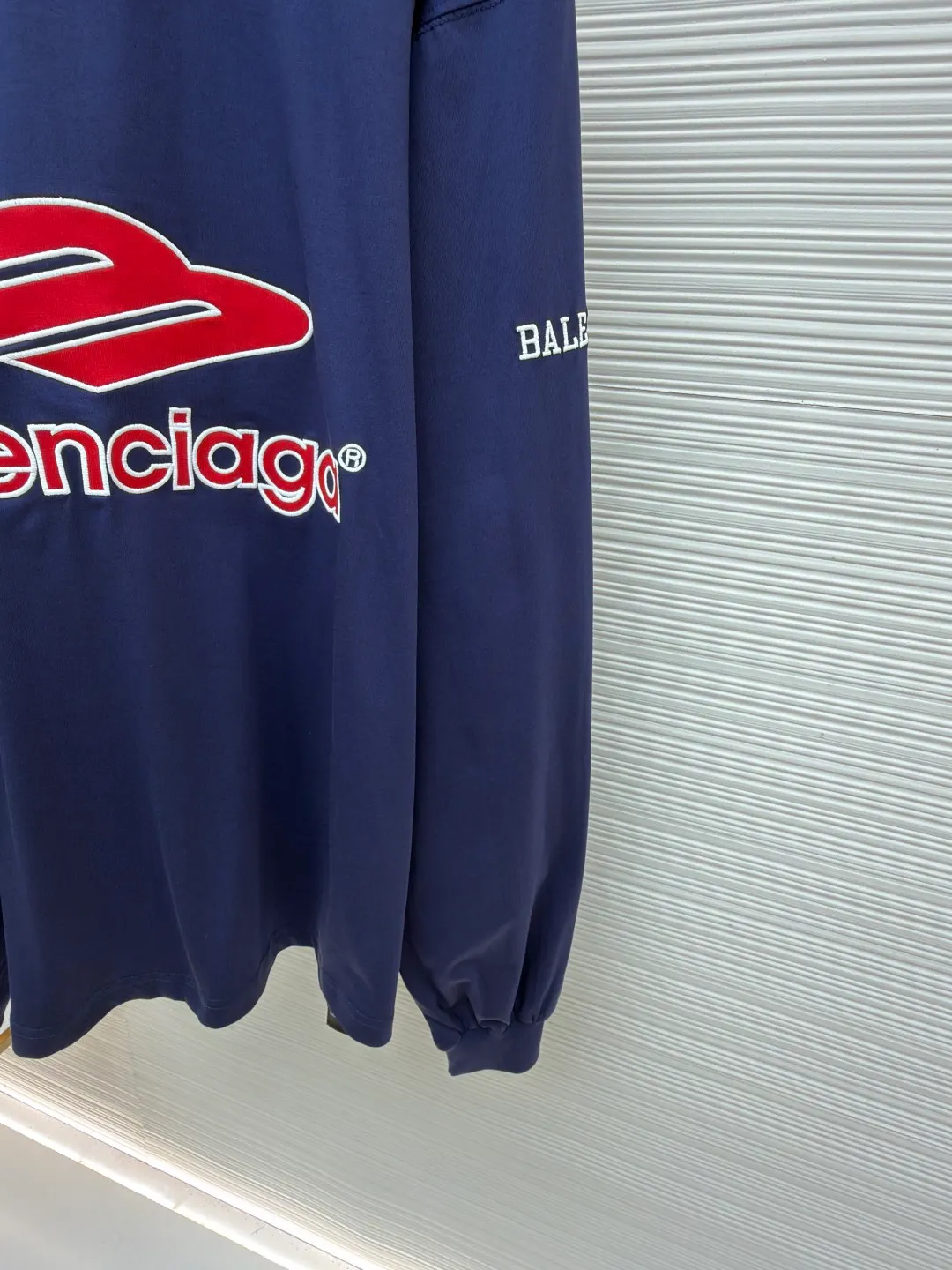 Balenciaga team series V-neck long sleeves ●Original version: purchased and developed by 8016 ●Item number: 1682072-A55 ●Fabric: plain knitted compact cotton fabric ●Technology: glue printing ●Color: blue ●Version: loose version ●Weight: about 375 grams ●Size: XS-S-M-L ●Description: The main body is made of 24-count special woven compact cotton with a weight of 185g/㎡. Compact spinning technology is applied in the spinning process, which significantly reduces yarn hairiness and makes the yarn smoother and stronger. This gives the fabric an unusually dense structure, a smooth and smooth surface, and excellent pilling resistance, while retaining the softness and breathability of pure cotton. The weight of 185g is light to middleweight, ensuring that the clothing is light, drapeable and can move freely. It is very suitable for creating a long-sleeved shirt that combines sportiness with daily comfort. The V-neck part is made of two different colors of high-elastic rib fabrics. The process step is to first weave ribbed belts of two colors separately, and then through precise cutting and splicing, form a V-shaped neckline with sharp color contrast. It breaks the monotony of the solid color body, uses strong color contrast to create a young and energetic visual focus, and optimizes the neck line. The pattern is pre-cut and formed into patches on fabrics of different materials or colors, and then covered on the body. Finally, high-density embroidery thread is used to fix the edges and outline the internal details. Its function is to create patterns with bright colors, strong texture contrast, three-dimensionality and durability. The edges of the pattern are strong and not easy to wear. A special elastic paste is screen-printed on the sleeves to create brightly colored patterns with a slightly coated feel. The elastic paste ensures that the printed area can stretch with the fabric without cracking. It forms a texture contrast between one flat and one convex with the three-dimensional sense of appliqué, which increases the interest and complexity of the design. The overall wiring is straight and delicate, the fabric is comfortable and soft, and the color is consistent without color difference. It can be matched with the same style to create a fashionable look and control various occasions. Customized accessories, complete with three standards, same style for men and women!