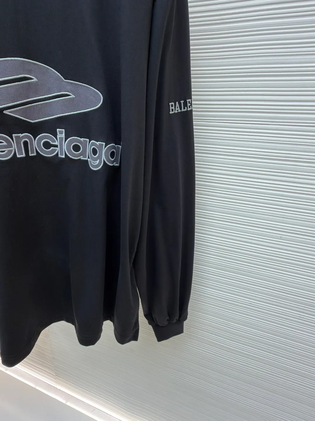 Balenciaga team series V-neck long sleeves ●Original version: purchased and developed by 8016 ●Item number: 1682073-A55 ●Fabric: plain knitted compact cotton fabric ●Technology: glue printing ●Color: black ●Version: loose version ●Weight: about 380 grams ●Size: XS-S-M-L ●Description: The main body is made of 24-count special woven compact cotton, with a weight of 185g/㎡. Compact spinning technology is applied in the spinning process, which significantly reduces yarn hairiness and makes the yarn smoother and stronger. This gives the fabric an unusually dense structure, a smooth and smooth surface, and excellent pilling resistance, while retaining the softness and breathability of pure cotton. The weight of 185g is light to middleweight, ensuring that the clothing is light, drapeable and can move freely. It is very suitable for creating a long-sleeved shirt that combines sportiness with daily comfort. The V-neck part is made of two different colors of high-elastic rib fabrics. The process step is to first weave ribbed belts of two colors separately, and then through precise cutting and splicing, form a V-shaped neckline with sharp color contrast. It breaks the monotony of the solid color body, uses strong color contrast to create a young and energetic visual focus, and optimizes the neck line. The pattern is pre-cut and formed into patches on fabrics of different materials or colors, and then covered on the body. Finally, high-density embroidery thread is used to fix the edges and outline the internal details. Its function is to create patterns with bright colors, strong texture contrast, three-dimensionality and durability. The edges of the pattern are strong and not easy to wear. A special elastic paste is screen-printed on the sleeves to create brightly colored patterns with a slightly coated feel. The elastic paste ensures that the printed area can stretch with the fabric without cracking. It forms a texture contrast between one flat and one convex with the three-dimensional sense of appliqué, which increases the interest and complexity of the design. The overall wiring is straight and delicate, the fabric is comfortable and soft, and the color is consistent without color difference. It can be matched with the same style to create a fashionable look and control various occasions. Customized accessories, complete with three standards, same style for men and women!