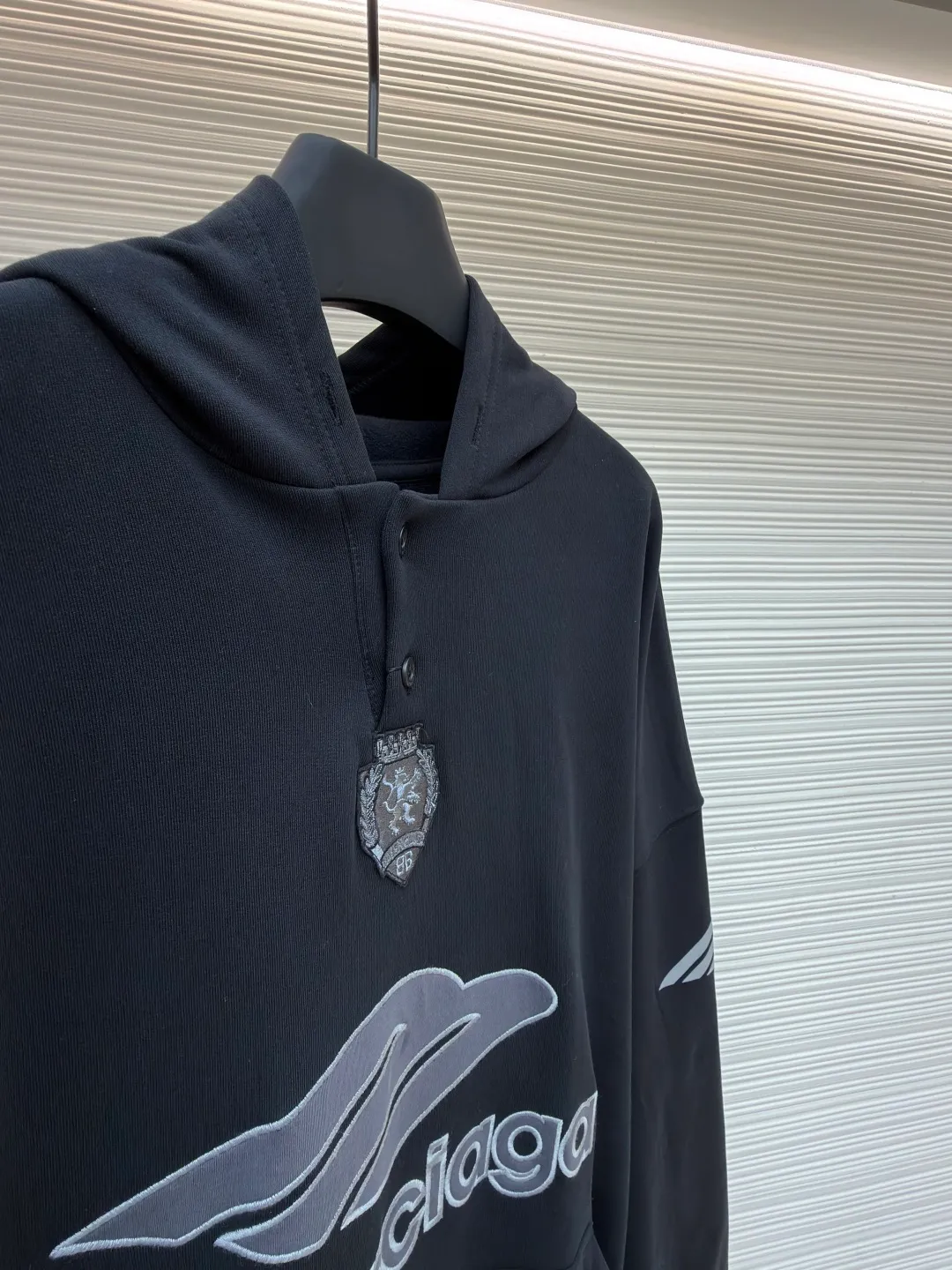 Balenciaga 3B football Polo hoodie ●Original version: Purchased and developed for 9999 ●Item number: 1681997-B40 ●Fabric: cotton fabric ●Technology: embroidery applique production ●Color: black ●Version: loose fit ●Weight: about 860 grams ●Size: XS-S-M-L ●Description: The neckline adopts a half-open button design and is decorated with metal badges to enhance the layered look; the main body of the garment presents the brand logo through three-dimensional foam printing technology, and the grayscale gradient effect enhances the visual texture. The cuffs and hem are edged with contrasting ribbing, which has moderate elasticity and is not easily deformed; a collage label is embedded in the left hem, and the details echo the brand's street style. The partial logo embroidery on the shoulders and cuffs echoes the main pattern. The overall craftsmanship takes into account practical wearability and brand recognition, making it suitable for daily casual or trendy looks. The overall wiring is straight and delicate, the fabric is comfortable and soft, and the color is consistent without color difference. It can be matched with the same style to create a fashionable look and control various occasions. Customized accessories, complete with three standards, same style for men and women!