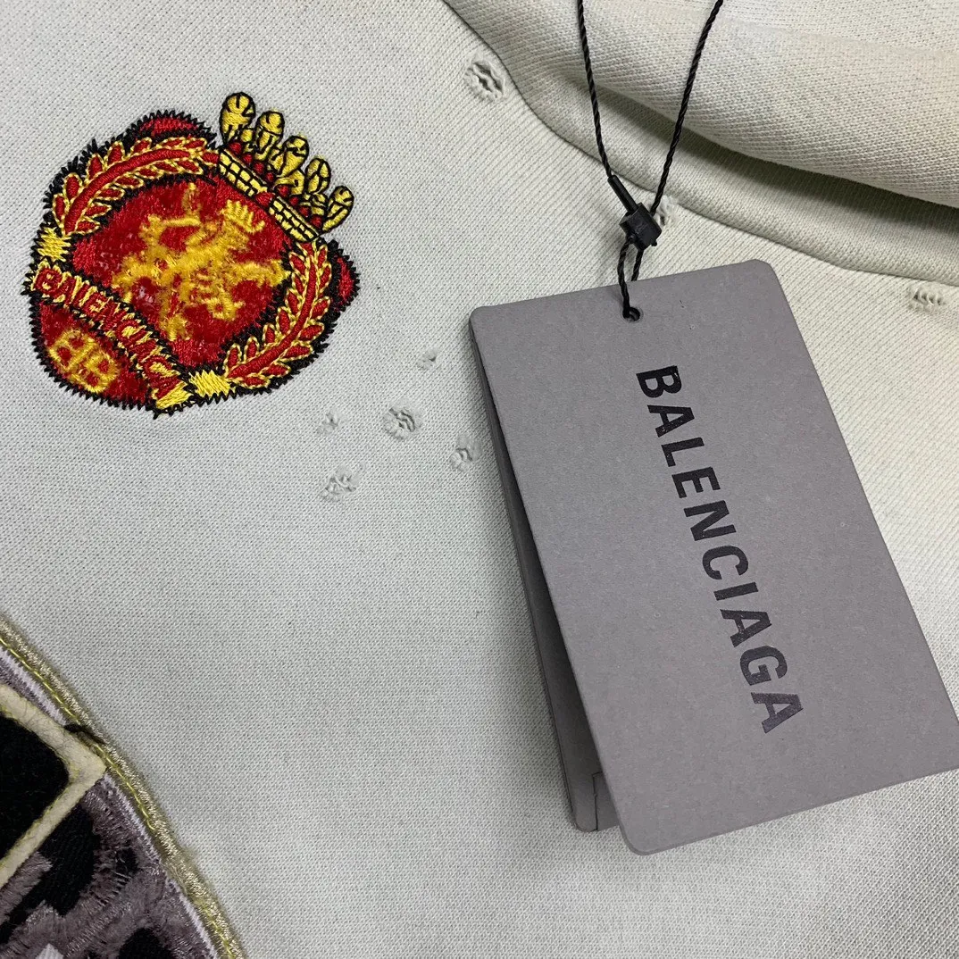 Additional details————Top-level verified version 23FW BALENCIAGA Paris Manchester United limited edition distressed male and female couple star same style pure cotton loose hooded sweatshirt [very suitable for Douyin, and other platforms! The letters in the LOGO position have been damaged and polished! 】 The fabric is custom-made washed knitted cotton terry material. The upper body is very soft. The front panel uses a classic hand pocket with a worn effect. The overall yellow and dirty effect is all artificially sprayed with majolica. It requires proficiency and experience to achieve this natural and elegant effect!  Customized towel embroidery on the chest, heavily damaged! The aging effect is very obvious! The overall artificial positioning coating is hand-made, washed and dirty. The frayed hole craftsmanship has a hand-painted graffiti effect. The arms behind the bend are made of open-stitch frayed craftsmanship. The wiring is delicate. Elastic cuff design. The whole body is hand-positioned with muddy dyeing and frayed effect! Ready-made garments are washed twice with water +➕ once with wax. It feels smooth!   The Manchester United letters and logo on the chest are designed with full embroidery and the details are visible!  Size: XS-L Color: White Black P: 470