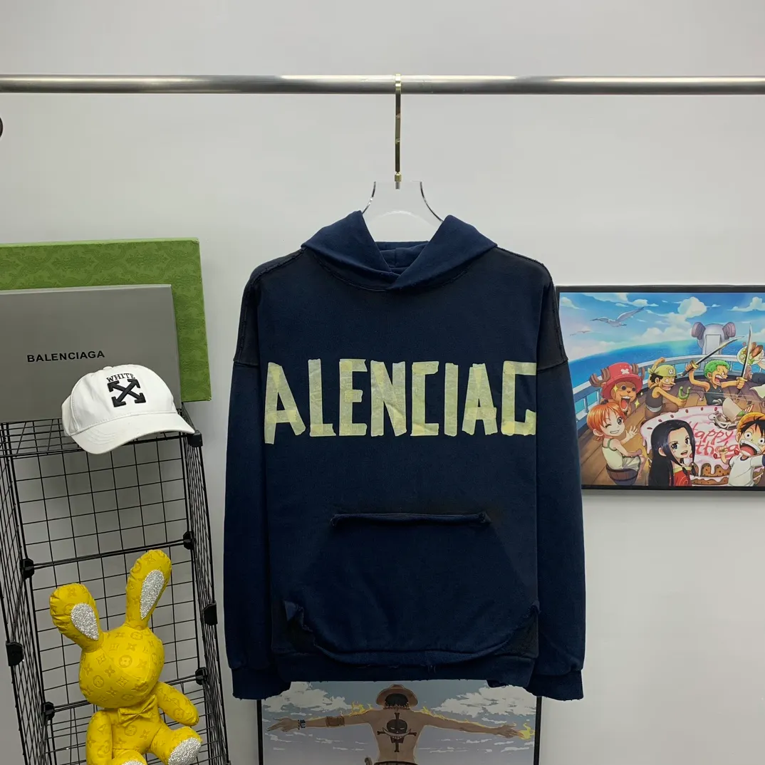 The top proven version of Balenciaga 23SS masking paper printed letters double-sided logo hooded loose hooded sweatshirt. This hoodie has a very interesting and cute design. The kangaroo pocket on the front of the large body is reverse-cut design. The double side pockets are hollow, which means that when viewed from the front, it actually deceives your vision. The real pockets are sewn on the reverse terry bottom. It is time-consuming and labor-intensive, but it is the core theme of the entire hoodie that cannot be ignored. The same detail is that the double side pockets are hemmed and stitched. And processed with holes; 480g heavy-weight pure cotton fabric with fine small terry bottom. After heavy mud dyeing and washing, the fabric still has a thick foundation and is comfortable and soft. The front and back double-sided textured paper transfer LOGO, and the front and back printing colors are different. The loose and large drop shoulder design is unisex. This style is also very suitable for girls to match. It is easy to create a lazy and casual street feel of the United States and France. Many holes are processed by hand grinding wheels on the body. Traces of muddying can be seen on the neckline, shoulder line, and side cuff splicing, but the visual effect transition is natural and soft without any sense of dirt. The old effect of the entire hoodie is excellent. The cuff threads are custom-woven in color; the packaging is washed and customized. The new gray silver letter main logo. The dropped shoulder model does not include shoulder width. The version is Kanye’s American style. Short and wide street casual version. From short sleeves to sweaters, this style is definitely not to be missed. Color: mud-dyed custom-woven navy Size: XS-S-M (Can be worn by both men and women, OS is loose and dropped on the shoulders) P:510