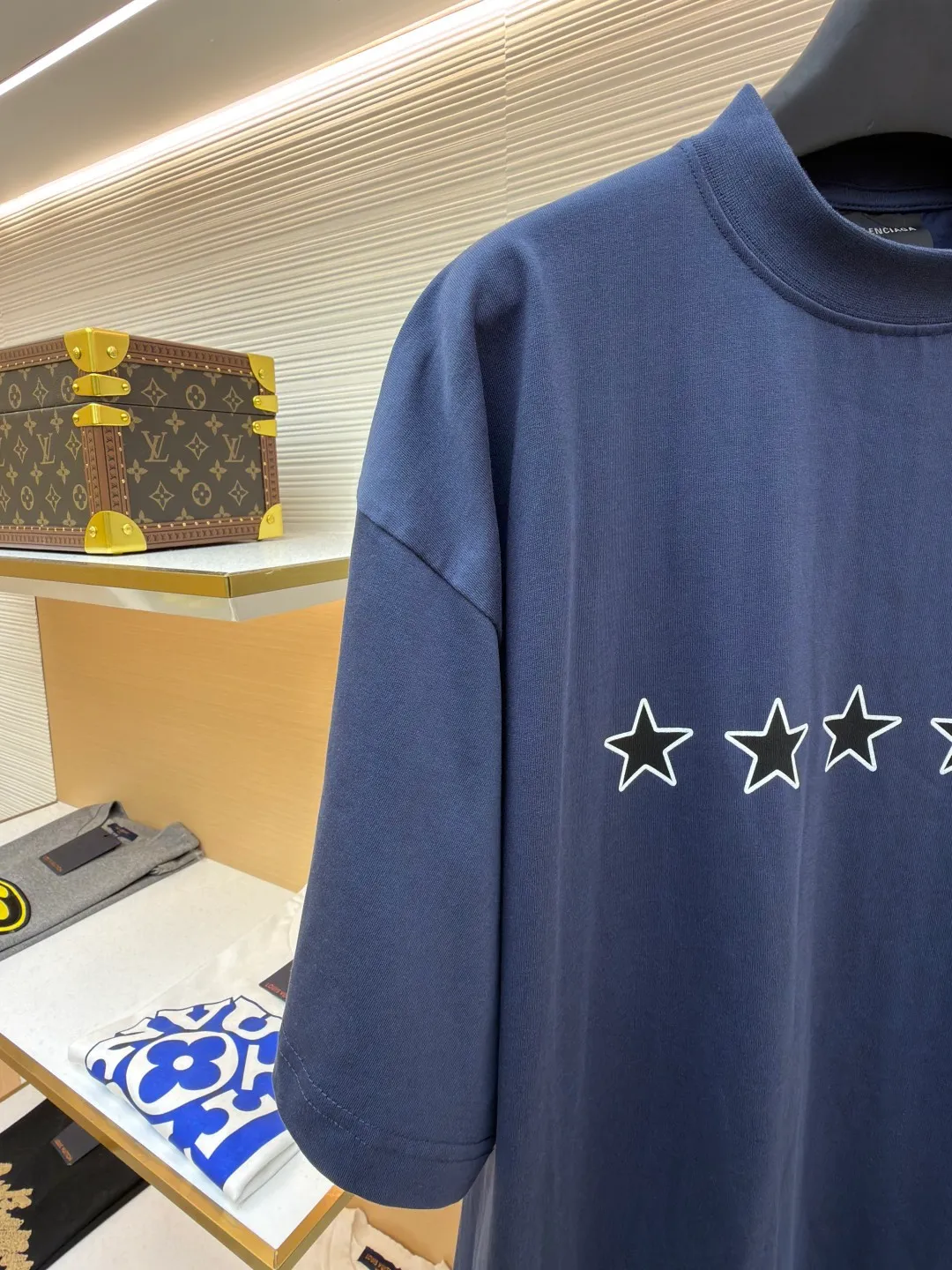 Balenciaga star embroidered short sleeves [comes with marker] ●Item number: 1682275-A20 ●Material: combed cotton fabric ●Technology: embroidery printing ●Color: blue ●Version: loose fit ●Weight: about 355 grams ●Size: XS-S-M-L ●Description: This navy blue short-sleeved T-shirt is made of high-density piqué mesh cotton fabric. The fabric has been custom-woven and dyed. The navy blue tone is uniform and not easy to fade. The breathable structure formed by the piqué texture makes the wearer more refreshing. At the same time, the fabric has excellent stiffness and can support the loose shoulder silhouette. The five-star pattern on the chest adopts double-track offset printing + inlay embroidery process. First, the outline of the stars is outlined with high-temperature embossing using matte silicone material. The thickness of the silicone layer is controlled at 0.3mm to ensure softness and no irritation to the skin. White embroidery thread is then used to fill in inlay along the edge of the silicone to give the star pattern a three-dimensional relief texture. The stitch density of each star reaches 12 stitches/cm, and the pattern alignment error does not exceed 0.1cm. The neckline is designed with a small stand-up collar, which is woven with ribs of the same fabric. It is not easy to loose after high-temperature pre-shrinking treatment. The side seams are spliced ​​with a seamless buried clip process to reduce friction when wearing. The overall process takes into account the texture and wearing comfort. The overall wiring is straight and delicate, the fabric is comfortable and soft, and the color is consistent without color difference. It can be matched with the same style to create a fashionable look and control various occasions. Customized accessories, complete with three standards, same style for men and women!