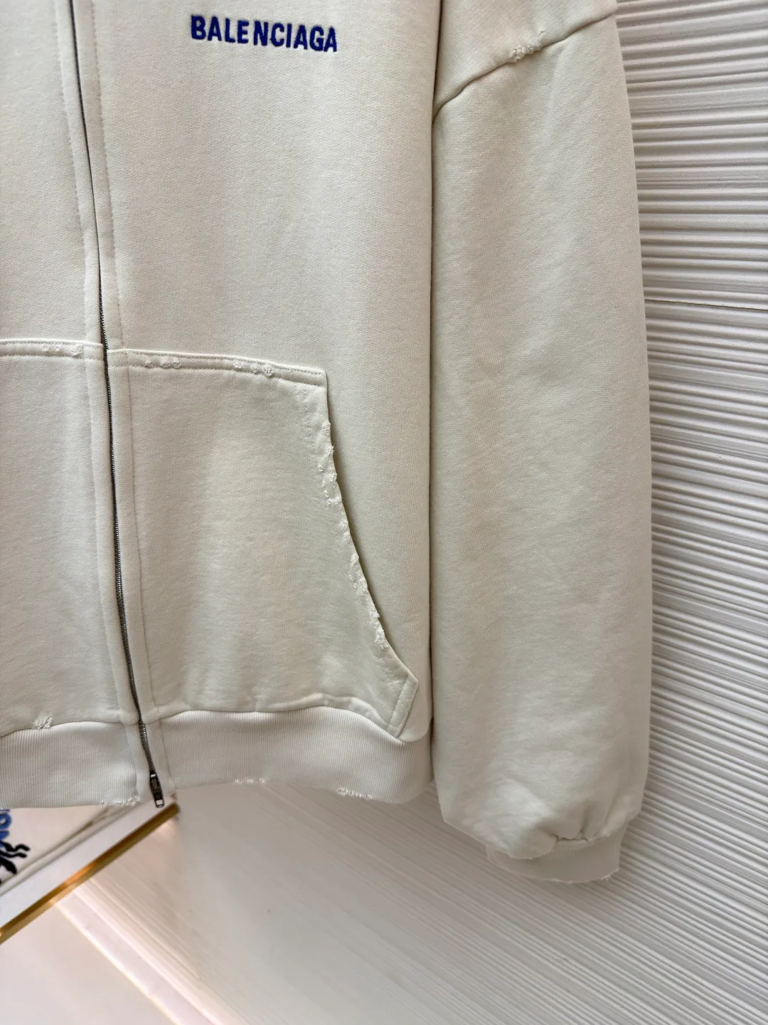 Balenciaga letter embroidered hooded zipper long-sleeved sweatshirt ●Original version: Purchased and developed for 9200 ●Item number: 1682263-A95 ●Fabric: combed cotton ●Technology: Washed and frayed ●Color: white ●Version: loose fit ●Weight: about 965 grams ●Size: S-M-L ●Description: This Balenciaga letter embroidered hooded zipper sweatshirt is made of 380g heavyweight pure cotton terry cloth, which has been treated with enzyme washing process. The fabric has a natural old-fashioned soft and waxy texture. At the same time, the stone grinding process is used to create irregular raw edge effects on the cuffs and hem, restoring the retro street style. The body adopts a loose, dropped-shoulder version, and the three-dimensional tailoring makes the shoulder lines smooth. The hooded part has a built-in drawstring made of pure cotton and is pre-shrunk to prevent it from deforming. The custom-made metal zipper on the front zipper closes smoothly and has no lag after repeated opening and closing tests. The brand letters on the left chest are made with imported embroidery machines using flat embroidery stitches, using polyester thread with high color fastness. The stitches are fine and neat without skipping, and the letter outline is three-dimensional and clear. The overall stitching uses double-needle overlocking technology, with up to 12 stitches per inch. The ribbed edges on the cuffs and hem are made of spandex blended material, which has long-lasting elasticity and is not easy to loosen, taking into account both wearing comfort and stiffness. The overall wiring is straight and delicate, the fabric is comfortable and soft, and the color is consistent without color difference. It can be matched with the same style to create a fashionable look and control various occasions. Customized accessories, complete with three standards, same style for men and women!