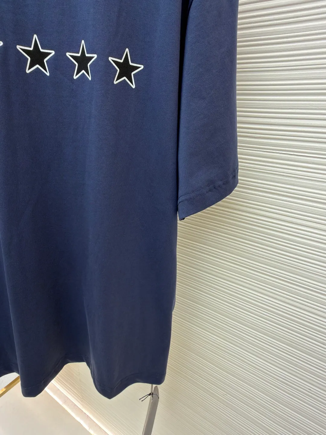 Balenciaga star embroidered short sleeves [comes with marker] ●Item number: 1682275-A20 ●Material: combed cotton fabric ●Technology: embroidery printing ●Color: blue ●Version: loose fit ●Weight: about 355 grams ●Size: XS-S-M-L ●Description: This navy blue short-sleeved T-shirt is made of high-density piqué mesh cotton fabric. The fabric has been custom-woven and dyed. The navy blue tone is uniform and not easy to fade. The breathable structure formed by the piqué texture makes the wearer more refreshing. At the same time, the fabric has excellent stiffness and can support the loose shoulder silhouette. The five-star pattern on the chest adopts double-track offset printing + inlay embroidery process. First, the outline of the stars is outlined with high-temperature embossing using matte silicone material. The thickness of the silicone layer is controlled at 0.3mm to ensure softness and no irritation to the skin. White embroidery thread is then used to fill in inlay along the edge of the silicone to give the star pattern a three-dimensional relief texture. The stitch density of each star reaches 12 stitches/cm, and the pattern alignment error does not exceed 0.1cm. The neckline is designed with a small stand-up collar, which is woven with ribs of the same fabric. It is not easy to loose after high-temperature pre-shrinking treatment. The side seams are spliced ​​with a seamless buried clip process to reduce friction when wearing. The overall process takes into account the texture and wearing comfort. The overall wiring is straight and delicate, the fabric is comfortable and soft, and the color is consistent without color difference. It can be matched with the same style to create a fashionable look and control various occasions. Customized accessories, complete with three standards, same style for men and women!