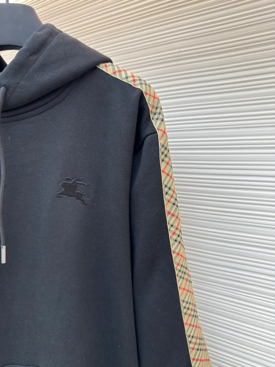 BURBERRY Ribbon trim hooded pullover sweatshirt ●Authentic product: Purchased and developed by 6239 ●Item number: 1680511-B15 ●Fabric: single-sided fish scale fabric ●Technology: selvedge production ●Version: fitted version ●Weight: about 895 grams ●Size: S-M-L-XL ●Description: A single-sided fish-scale cloth fabric woven with cotton as the base. The front is a smooth knitted surface, and the skin-contacting surface is formed into three-dimensional terry by the floating thread knitting technology of the knitting machine, which increases the fluffiness and has a delicate touch. The terry structure absorbs a large amount of water and evaporates quickly, so it is not easy to loosen and deform after repeated washing. By actively interfering with the shrinkage potential of cotton fibers, the fabric is able to transition from changeable to stable, improving dimensional stability while being less prone to deformation and wrinkles. The monochrome flat embroidery on the chest uses the high-precision calculation system of the computer embroidery machine to control the coordinated operation of the machine head, needle bar, and thread spool. The fabric frame moves accurately in the horizontal and vertical directions to form a stitch track. The upper and lower thread tensions are adjusted to ensure that the stitches are smooth and free of floating threads, forming a fine pattern with an error of ±0.1mm. The overall wiring is straight and delicate, the fabric is comfortable and soft, and the color is consistent without color difference. It can be matched with the same style to create a fashionable look and control various occasions. Customized accessories, complete with three standards, same style for men and women!