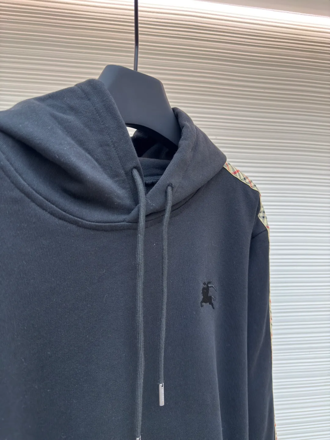 BURBERRY Ribbon trim hooded pullover sweatshirt ●Authentic product: Purchased and developed by 6239 ●Item number: 1680511-B15 ●Fabric: single-sided fish scale fabric ●Technology: selvedge production ●Version: fitted version ●Weight: about 895 grams ●Size: S-M-L-XL ●Description: A single-sided fish-scale cloth fabric woven with cotton as the base. The front is a smooth knitted surface, and the skin-contacting surface is formed into three-dimensional terry by the floating thread knitting technology of the knitting machine, which increases the fluffiness and has a delicate touch. The terry structure absorbs a large amount of water and evaporates quickly, so it is not easy to loosen and deform after repeated washing. By actively interfering with the shrinkage potential of cotton fibers, the fabric is able to transition from changeable to stable, improving dimensional stability while being less prone to deformation and wrinkles. The monochrome flat embroidery on the chest uses the high-precision calculation system of the computer embroidery machine to control the coordinated operation of the machine head, needle bar, and thread spool. The fabric frame moves accurately in the horizontal and vertical directions to form a stitch track. The upper and lower thread tensions are adjusted to ensure that the stitches are smooth and free of floating threads, forming a fine pattern with an error of ±0.1mm. The overall wiring is straight and delicate, the fabric is comfortable and soft, and the color is consistent without color difference. It can be matched with the same style to create a fashionable look and control various occasions. Customized accessories, complete with three standards, same style for men and women!