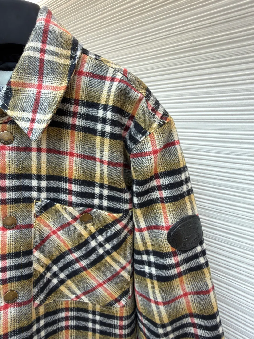 Burberry plaid wool lapel cotton coat ●Original version: Purchased and developed by 7353 ●Item number: 1681919-B40 ●Fabric: wool blended fabric ●Technology: Made on positioning cutting machine ●Color: Khaki ●Version: Fitted version ●Weight: about 800 grams ●Size: S-M-L-XL ●Description: This plaid shirt-style jacket is made of mixed-color wool blend fabric. It is combed to enhance the velvet feel and warmth, and the surface presents a natural variegated texture. The plaid pattern is based on khaki, with gray and red contrasting lines superimposed. The positioning printing process ensures that the plaid pattern is aligned when the pieces are spliced. The placket is made of vintage metal snaps, which are wear-resistant and have a thick texture; the left chest patch pocket is designed with diagonal splicing, and the bag mouth is reinforced with double-line sewing. The neckline is a classic lapel with seamed edges; the cuffs are single-button adjustable, and the inner lining is made of cotton of the same color to improve wearing comfort. The overall stitching density reaches 12 stitches/inch, and the double hemming process on the hem enhances durability. It is suitable for layering or single wear in autumn and winter. The overall wiring is straight and delicate, the fabric is comfortable and soft, and the color is consistent without color difference. It can be matched with the same style to create a fashionable look and control various occasions. Customized accessories, complete with three standards, same style for men and women!