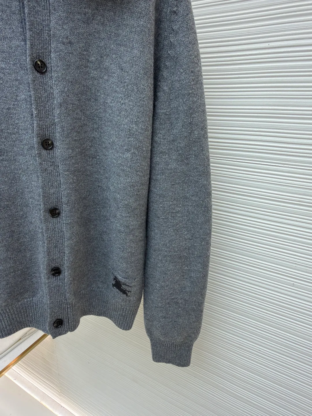 Burberry lapel rib knitted cashmere sweater ●Original version: purchased and developed by 11575 ●Item number: 1682227-B15 ●Fabric: wool blended fabric ●Technology: knitted ●Color: gray ●Version: fitted version ●Weight: about 580 grams ●Size: S-M-L-XL ●Description: This black knitted cardigan is knitted with high-count worsted wool yarn. The main body is built using four-flat stitch technology, which gives the fabric good elasticity and shapeability, while forming a fine and tight texture. The ribbed lapel weaving process is used at the neckline, and a combination of different needle types is used to create a crisp collar profile. The rib structure can be freely expanded and contracted according to the wearing status to fit the neck line. The placket adopts inlaid buttonhole technology and is matched with matte resin buttons of the same color. The buttons and the body are fixed by hand-stitching, which is strong and beautiful. The brand logo patch on the lower side of the body is processed by a hot-pressing bonding process and fits seamlessly with the knitted fabric. The overall cut is a slightly loose shoulder-drop version, combined with three-dimensional darting technology, which ensures wearing comfort while creating clean lines. Every knitting node is manually inspected to ensure the uniformity and integrity of the knitted texture. The overall wiring is straight and delicate, the fabric is comfortable and soft, and the color is consistent without color difference. It can be matched with the same style to create a fashionable look and control various occasions. Customized accessories, complete with three standards, same style for men and women!