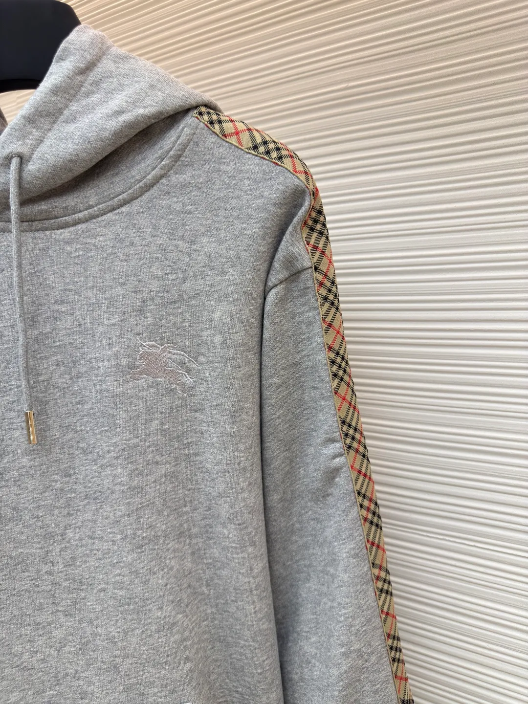 BURBERRY Ribbon trim hooded pullover sweatshirt ●Authentic product: Purchased and developed by 6239 ●Item number: 1680510-B15 ●Fabric: single-sided fish scale fabric ●Technology: selvedge production ●Version: fitted version ●Weight: about 855 grams ●Size: S-M-L-XL ●Description: A single-sided fish-scale cloth fabric woven with cotton as the base. The front is a smooth knitted surface, and the skin-contacting surface is formed into three-dimensional terry by the floating thread knitting technology of the knitting machine, which increases the fluffiness and has a delicate touch. The terry structure absorbs a large amount of water and evaporates quickly, so it is not easy to loosen and deform after repeated washing. By actively interfering with the shrinkage potential of cotton fibers, the fabric is able to transition from changeable to stable, improving dimensional stability while being less prone to deformation and wrinkles. The monochrome flat embroidery on the chest uses the high-precision calculation system of the computer embroidery machine to control the coordinated operation of the machine head, needle bar, and thread spool. The fabric frame moves accurately in the horizontal and vertical directions to form a stitch track. The upper and lower thread tensions are adjusted to ensure that the stitches are smooth and free of floating threads, forming a fine pattern with an error of ±0.1mm. The overall wiring is straight and delicate, the fabric is comfortable and soft, and the color is consistent without color difference. It can be matched with the same style to create a fashionable look and control various occasions. Customized accessories, complete with three standards, same style for men and women!