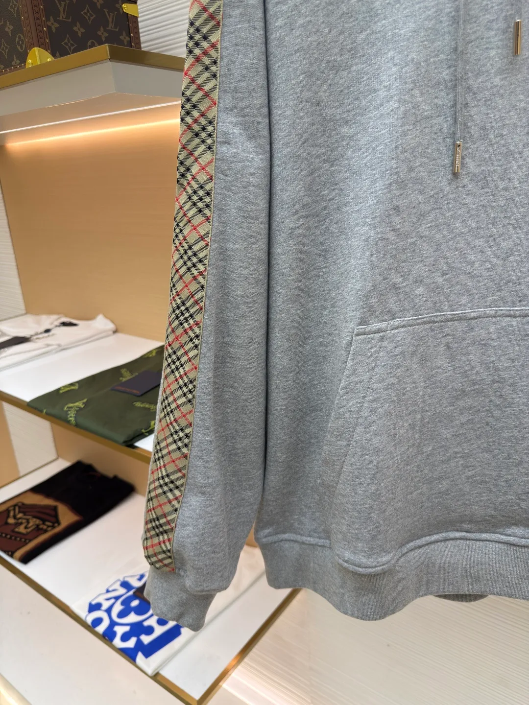 BURBERRY Ribbon trim hooded pullover sweatshirt ●Authentic product: Purchased and developed by 6239 ●Item number: 1680510-B15 ●Fabric: single-sided fish scale fabric ●Technology: selvedge production ●Version: fitted version ●Weight: about 855 grams ●Size: S-M-L-XL ●Description: A single-sided fish-scale cloth fabric woven with cotton as the base. The front is a smooth knitted surface, and the skin-contacting surface is formed into three-dimensional terry by the floating thread knitting technology of the knitting machine, which increases the fluffiness and has a delicate touch. The terry structure absorbs a large amount of water and evaporates quickly, so it is not easy to loosen and deform after repeated washing. By actively interfering with the shrinkage potential of cotton fibers, the fabric is able to transition from changeable to stable, improving dimensional stability while being less prone to deformation and wrinkles. The monochrome flat embroidery on the chest uses the high-precision calculation system of the computer embroidery machine to control the coordinated operation of the machine head, needle bar, and thread spool. The fabric frame moves accurately in the horizontal and vertical directions to form a stitch track. The upper and lower thread tensions are adjusted to ensure that the stitches are smooth and free of floating threads, forming a fine pattern with an error of ±0.1mm. The overall wiring is straight and delicate, the fabric is comfortable and soft, and the color is consistent without color difference. It can be matched with the same style to create a fashionable look and control various occasions. Customized accessories, complete with three standards, same style for men and women!