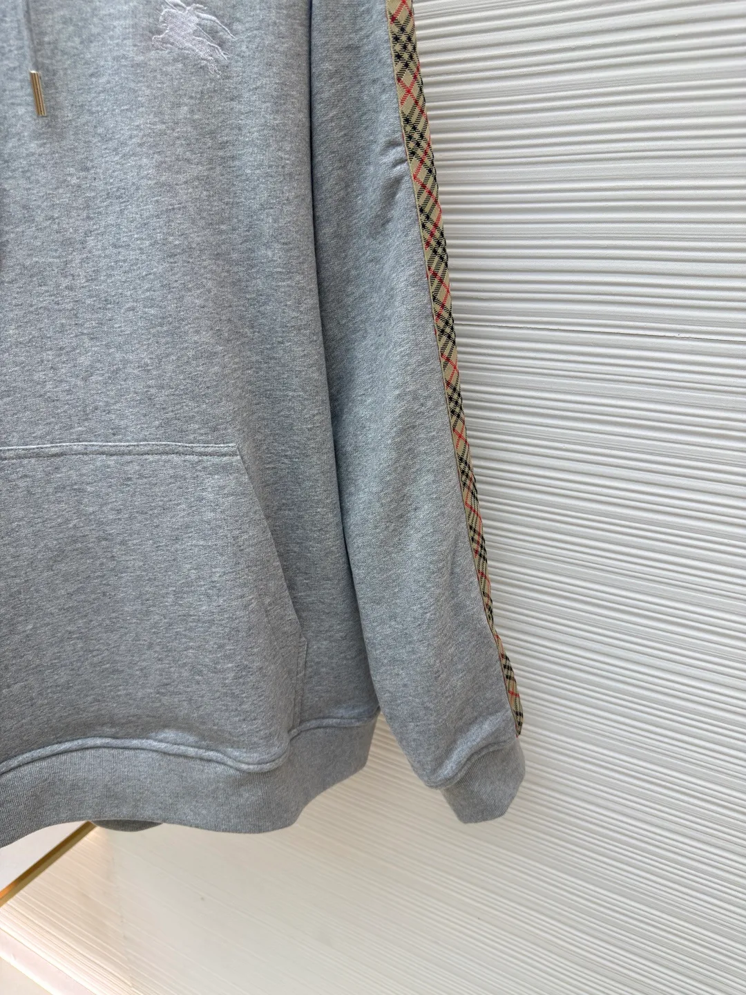 BURBERRY Ribbon trim hooded pullover sweatshirt ●Authentic product: Purchased and developed by 6239 ●Item number: 1680510-B15 ●Fabric: single-sided fish scale fabric ●Technology: selvedge production ●Version: fitted version ●Weight: about 855 grams ●Size: S-M-L-XL ●Description: A single-sided fish-scale cloth fabric woven with cotton as the base. The front is a smooth knitted surface, and the skin-contacting surface is formed into three-dimensional terry by the floating thread knitting technology of the knitting machine, which increases the fluffiness and has a delicate touch. The terry structure absorbs a large amount of water and evaporates quickly, so it is not easy to loosen and deform after repeated washing. By actively interfering with the shrinkage potential of cotton fibers, the fabric is able to transition from changeable to stable, improving dimensional stability while being less prone to deformation and wrinkles. The monochrome flat embroidery on the chest uses the high-precision calculation system of the computer embroidery machine to control the coordinated operation of the machine head, needle bar, and thread spool. The fabric frame moves accurately in the horizontal and vertical directions to form a stitch track. The upper and lower thread tensions are adjusted to ensure that the stitches are smooth and free of floating threads, forming a fine pattern with an error of ±0.1mm. The overall wiring is straight and delicate, the fabric is comfortable and soft, and the color is consistent without color difference. It can be matched with the same style to create a fashionable look and control various occasions. Customized accessories, complete with three standards, same style for men and women!