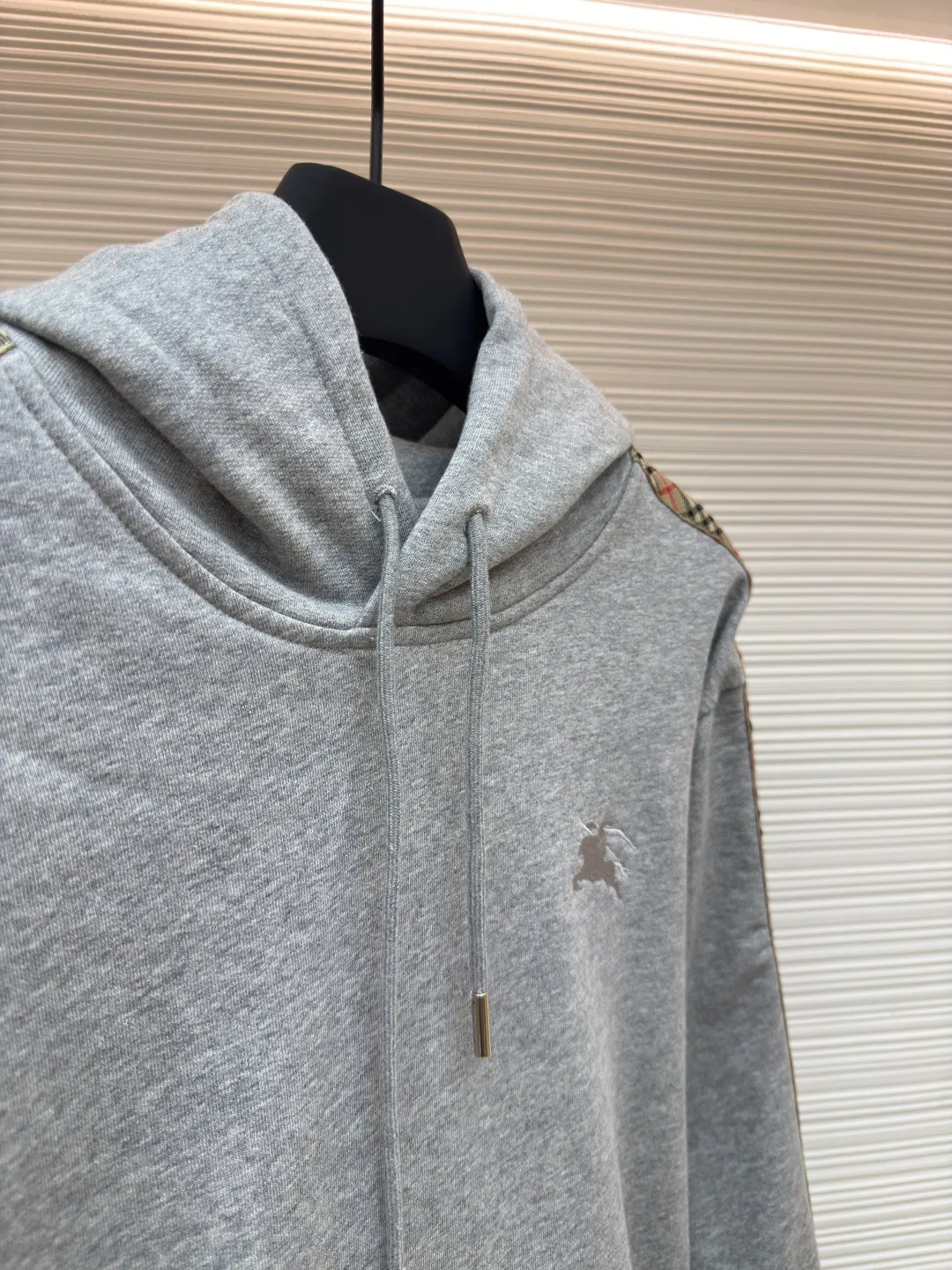BURBERRY Ribbon trim hooded pullover sweatshirt ●Authentic product: Purchased and developed by 6239 ●Item number: 1680510-B15 ●Fabric: single-sided fish scale fabric ●Technology: selvedge production ●Version: fitted version ●Weight: about 855 grams ●Size: S-M-L-XL ●Description: A single-sided fish-scale cloth fabric woven with cotton as the base. The front is a smooth knitted surface, and the skin-contacting surface is formed into three-dimensional terry by the floating thread knitting technology of the knitting machine, which increases the fluffiness and has a delicate touch. The terry structure absorbs a large amount of water and evaporates quickly, so it is not easy to loosen and deform after repeated washing. By actively interfering with the shrinkage potential of cotton fibers, the fabric is able to transition from changeable to stable, improving dimensional stability while being less prone to deformation and wrinkles. The monochrome flat embroidery on the chest uses the high-precision calculation system of the computer embroidery machine to control the coordinated operation of the machine head, needle bar, and thread spool. The fabric frame moves accurately in the horizontal and vertical directions to form a stitch track. The upper and lower thread tensions are adjusted to ensure that the stitches are smooth and free of floating threads, forming a fine pattern with an error of ±0.1mm. The overall wiring is straight and delicate, the fabric is comfortable and soft, and the color is consistent without color difference. It can be matched with the same style to create a fashionable look and control various occasions. Customized accessories, complete with three standards, same style for men and women!