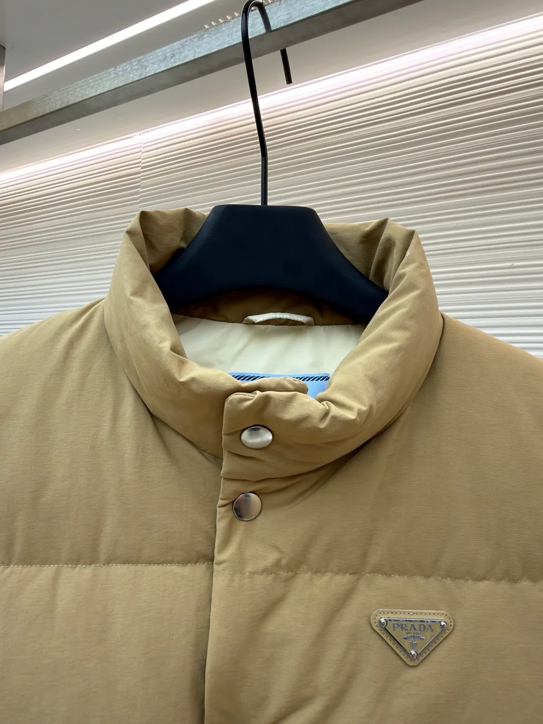 Prada stand collar badge down vest ●Original version: purchased and developed by 18756 ●Item number: 16801377-C30 ●Fabric: white duck down fabric ●Technology: mechanical down filling ●Color: khaki ●Version: Fitted version ●Weight: about 700 grams ●Size: S-M-L-XL ●Description: This vest is made of high-quality water-repellent fabric, and the khaki tone shows the texture. Using three-dimensional quilting technology, the down is evenly divided into full grid-shaped down-filled areas, which not only ensures warmth but also makes the silhouette crisp and three-dimensional. The neckline is designed with a stand-up collar and is matched with a metal snap placket, which is exquisite in texture and easy to put on and take off.  The front chest is decorated with the brand's iconic metal triangle logo, which is highly recognizable; the large patch pockets on both sides are three-dimensionally cut, and the bag mouth is in an inverted trapezoid shape, combining practicality and design. There is a built-in drawstring at the hem, and the tightness can be adjusted freely to suit different wear needs. From fabric selection to detail sewing, every process reflects the brand's strict control of craftsmanship, exquisitely integrating functionality and fashion sense. The overall wiring is straight and delicate, the fabric is comfortable and soft, and the color is consistent without color difference. It can be matched with the same style to create a fashionable look and control various occasions. Customized accessories, complete with three standards, same style for men and women!