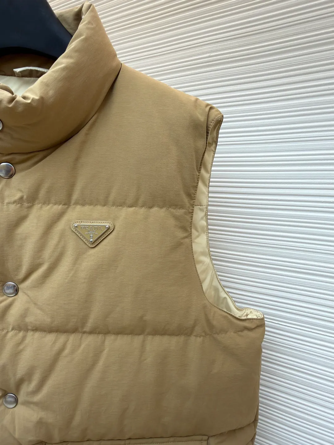 Prada stand collar badge down vest ●Original version: purchased and developed by 18756 ●Item number: 16801377-C30 ●Fabric: white duck down fabric ●Technology: mechanical down filling ●Color: khaki ●Version: Fitted version ●Weight: about 700 grams ●Size: S-M-L-XL ●Description: This vest is made of high-quality water-repellent fabric, and the khaki tone shows the texture. Using three-dimensional quilting technology, the down is evenly divided into full grid-shaped down-filled areas, which not only ensures warmth but also makes the silhouette crisp and three-dimensional. The neckline is designed with a stand-up collar and is matched with a metal snap placket, which is exquisite in texture and easy to put on and take off.  The front chest is decorated with the brand's iconic metal triangle logo, which is highly recognizable; the large patch pockets on both sides are three-dimensionally cut, and the bag mouth is in an inverted trapezoid shape, combining practicality and design. There is a built-in drawstring at the hem, and the tightness can be adjusted freely to suit different wear needs. From fabric selection to detail sewing, every process reflects the brand's strict control of craftsmanship, exquisitely integrating functionality and fashion sense. The overall wiring is straight and delicate, the fabric is comfortable and soft, and the color is consistent without color difference. It can be matched with the same style to create a fashionable look and control various occasions. Customized accessories, complete with three standards, same style for men and women!
