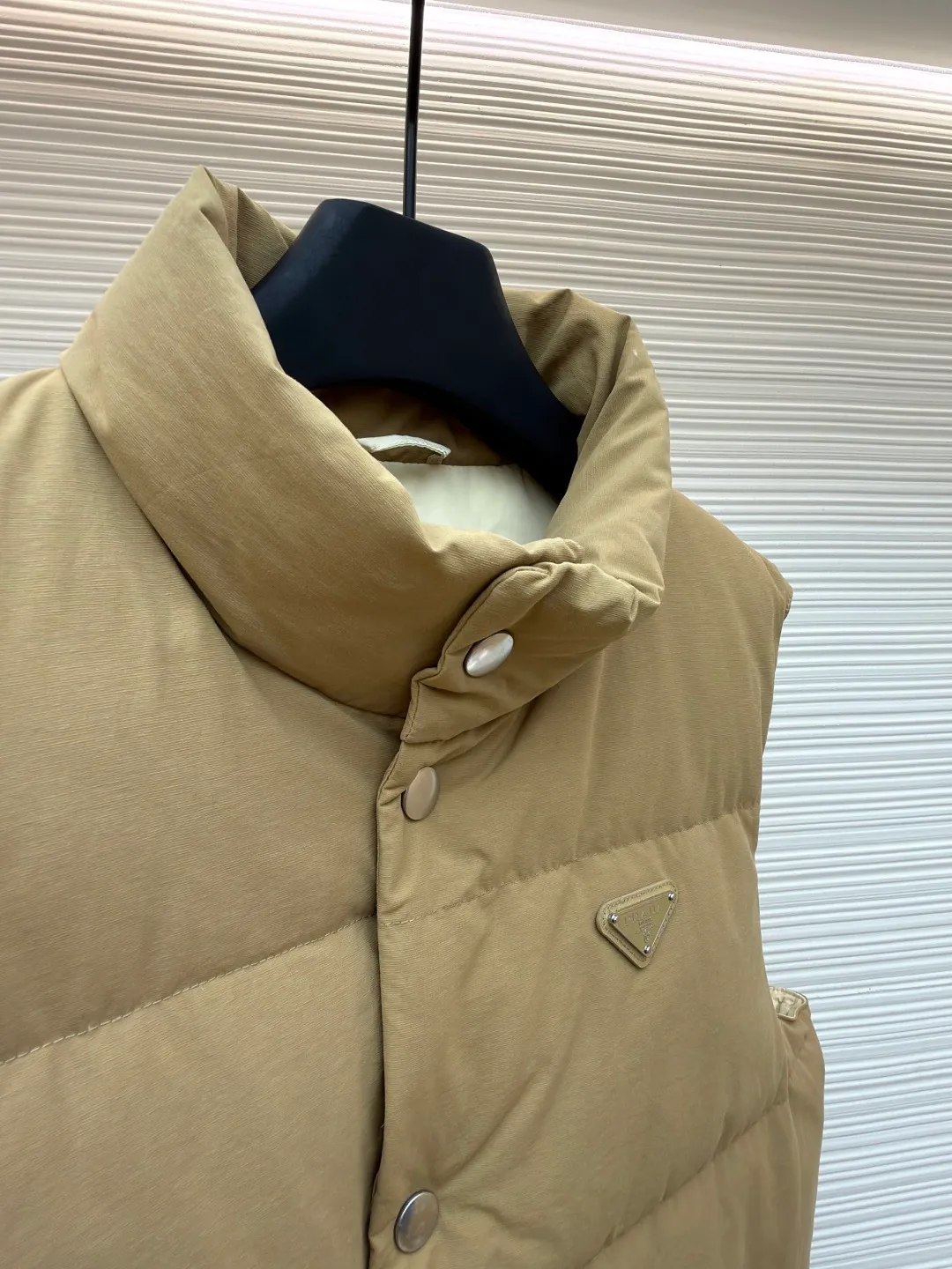 Prada stand collar badge down vest ●Original version: purchased and developed by 18756 ●Item number: 16801377-C30 ●Fabric: white duck down fabric ●Technology: mechanical down filling ●Color: khaki ●Version: Fitted version ●Weight: about 700 grams ●Size: S-M-L-XL ●Description: This vest is made of high-quality water-repellent fabric, and the khaki tone shows the texture. Using three-dimensional quilting technology, the down is evenly divided into full grid-shaped down-filled areas, which not only ensures warmth but also makes the silhouette crisp and three-dimensional. The neckline is designed with a stand-up collar and is matched with a metal snap placket, which is exquisite in texture and easy to put on and take off.  The front chest is decorated with the brand's iconic metal triangle logo, which is highly recognizable; the large patch pockets on both sides are three-dimensionally cut, and the bag mouth is in an inverted trapezoid shape, combining practicality and design. There is a built-in drawstring at the hem, and the tightness can be adjusted freely to suit different wear needs. From fabric selection to detail sewing, every process reflects the brand's strict control of craftsmanship, exquisitely integrating functionality and fashion sense. The overall wiring is straight and delicate, the fabric is comfortable and soft, and the color is consistent without color difference. It can be matched with the same style to create a fashionable look and control various occasions. Customized accessories, complete with three standards, same style for men and women!