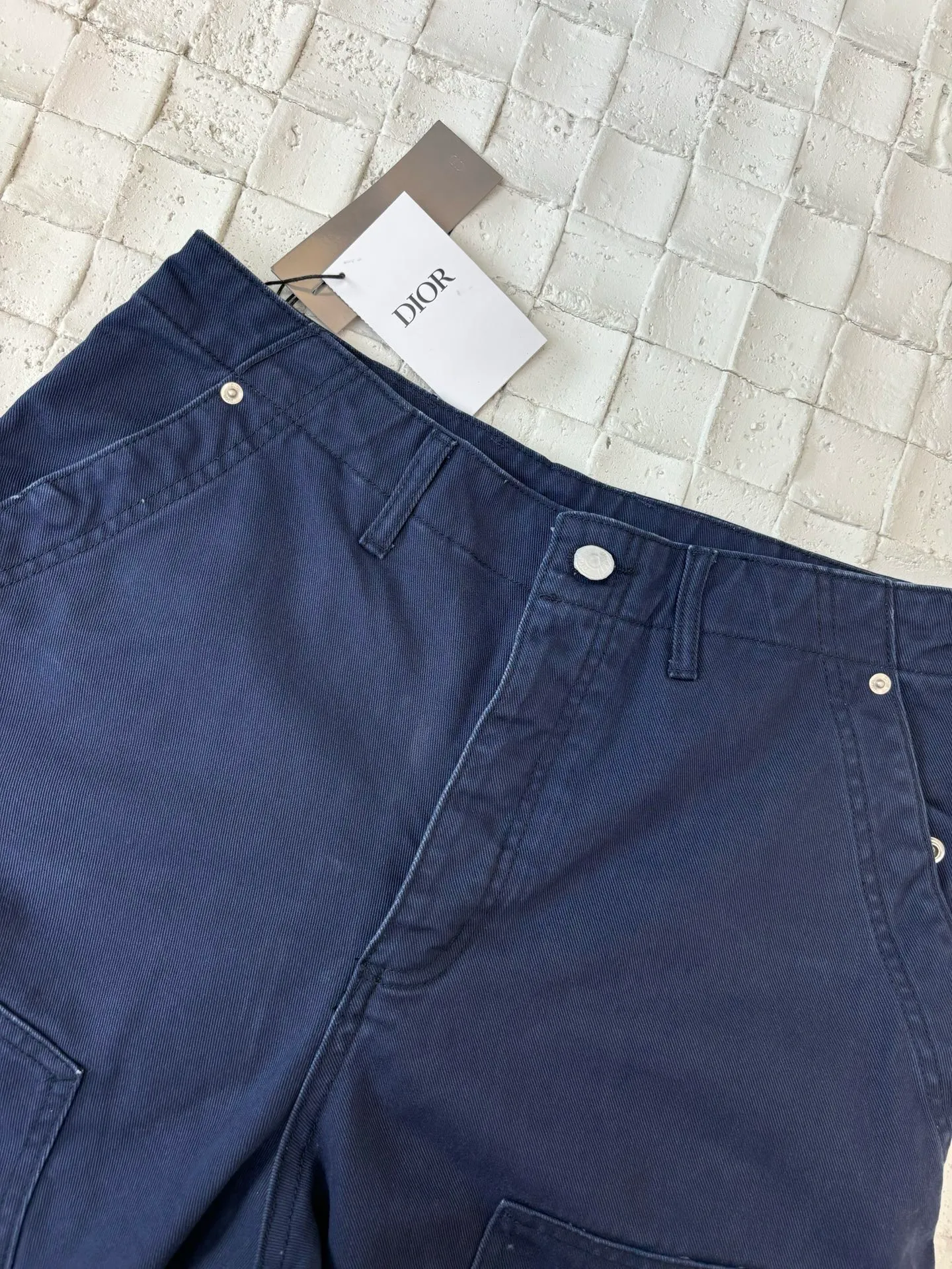 🅿️550 Dio*/Dior 25Fw new workwear blue logging French work pants. Customized twill denim (fixed dyed blue-purple) twill weaving structure. The yarn is customized using long-staple cotton + trace elastic fiber (≤3%) blend. Through the ring spinning + siro spinning composite process, the yarn has high strength and delicate surface. Pre-dyed yarn, cotton yarn is first dip-dyed with indigo 6 times (3-4 times for ordinary jeans) to ensure that the core layer is dyed through. The post-finishing uses nano-scale fixatives to give the blue a deep-sea gradient effect.   The front panel is three-dimensionally spliced, and the five-piece structure of traditional overalls is disassembled into nine asymmetrical pieces. The ergonomic curves are determined through 3D laser scanning. Double-needle differential feeding is used at the seam bone (spacing 2.5mm) to ensure no cracking during stretching.    The back leather is made of calfskin from HAAS leather factory, which is vegetable tanned and hand-rubbed to give it a matte lizard texture. Environmentally friendly dyeing uses water-based dyes, and the edge of the leather label is processed with burnt edge sealing to prevent burrs.    Size: 48/50/52