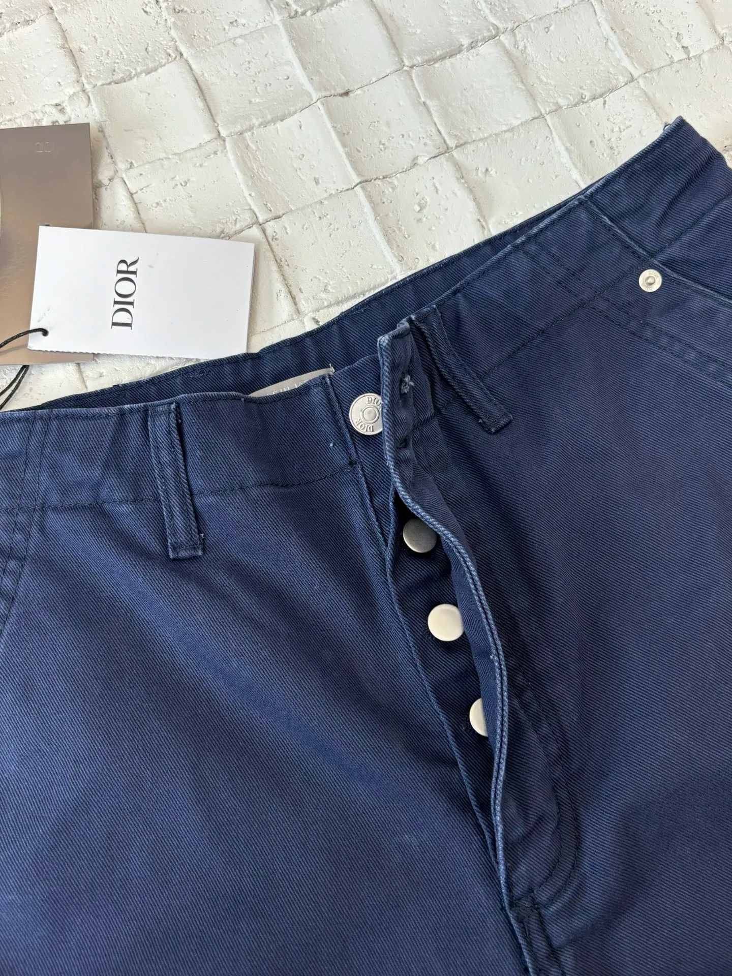 🅿️550 Dio*/Dior 25Fw new workwear blue logging French work pants. Customized twill denim (fixed dyed blue-purple) twill weaving structure. The yarn is customized using long-staple cotton + trace elastic fiber (≤3%) blend. Through the ring spinning + siro spinning composite process, the yarn has high strength and delicate surface. Pre-dyed yarn, cotton yarn is first dip-dyed with indigo 6 times (3-4 times for ordinary jeans) to ensure that the core layer is dyed through. The post-finishing uses nano-scale fixatives to give the blue a deep-sea gradient effect.   The front panel is three-dimensionally spliced, and the five-piece structure of traditional overalls is disassembled into nine asymmetrical pieces. The ergonomic curves are determined through 3D laser scanning. Double-needle differential feeding is used at the seam bone (spacing 2.5mm) to ensure no cracking during stretching.    The back leather is made of calfskin from HAAS leather factory, which is vegetable tanned and hand-rubbed to give it a matte lizard texture. Environmentally friendly dyeing uses water-based dyes, and the edge of the leather label is processed with burnt edge sealing to prevent burrs.    Size: 48/50/52