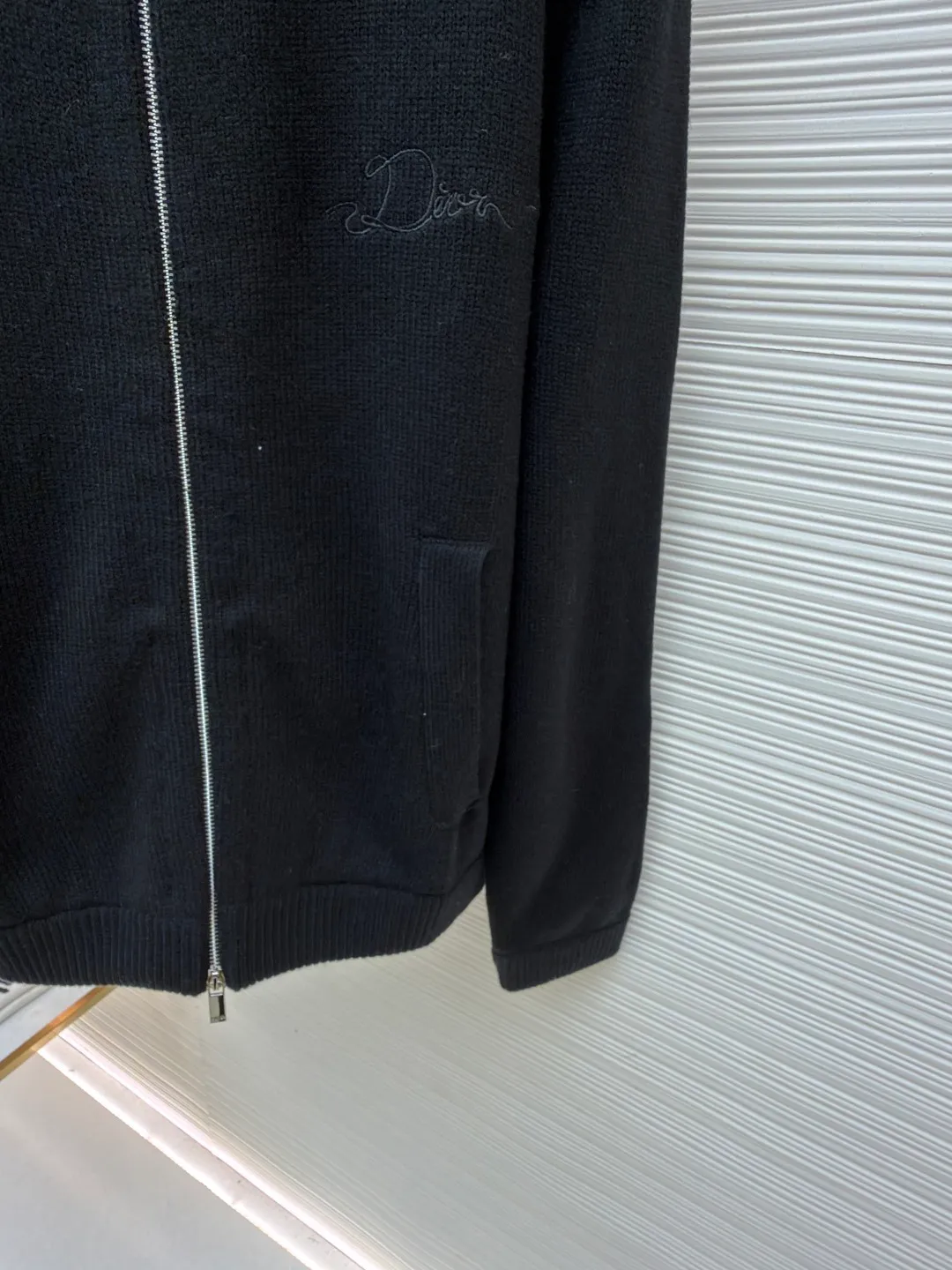 Dior letter embroidered wool knitted cardigan ●Original version: Purchased and developed by 18684 ●Item number: 1682138-C05 ●Fabric: wool blended fabric ●Technology: knitting ●Color: black ●Version: fitted version ●Weight: about 755 grams ●Size: S-M-L-XL ●Description: This Dior black knitted zipper cardigan is made of high-count worsted wool and mulberry silk blended yarn. It is woven with plain knitting technology on an Italian 16-needle computerized flat machine. The yarn is first treated with anti-pilling and pre-shrunk to make the garment soft and resistant to deformation. The Dior logo on the front chest adopts dark embroidery technology, using matte embroidery thread of the same color, completed with 0.1mm fine stitching, which is low-key and rich in texture; the three-dimensional Dior letters on the back use hand-made rope embroidery techniques, and the woven rope straps are fixed segment by section according to the outline of the version, forming a 3D relief effect. The connection between the rope strap and the body adopts invisible locking technology, without any abrupt threads. The inner side of the collar is spliced ​​with breathable mesh fabric, the metal zipper is made of custom matte nickel material, and the teeth are treated with wear-resistant treatment. The ribbed edges of the cuffs and hem have built-in elastic spandex yarn, and are hand-ironed and shaped. Every craftsmanship detail is in line with Dior's high-end ready-to-wear production standards. The overall wiring is straight and delicate, the fabric is comfortable and soft, and the color is consistent without color difference. It can be matched with the same style to create a fashionable look and control various occasions. Customized accessories, complete with three standards, same style for men and women!