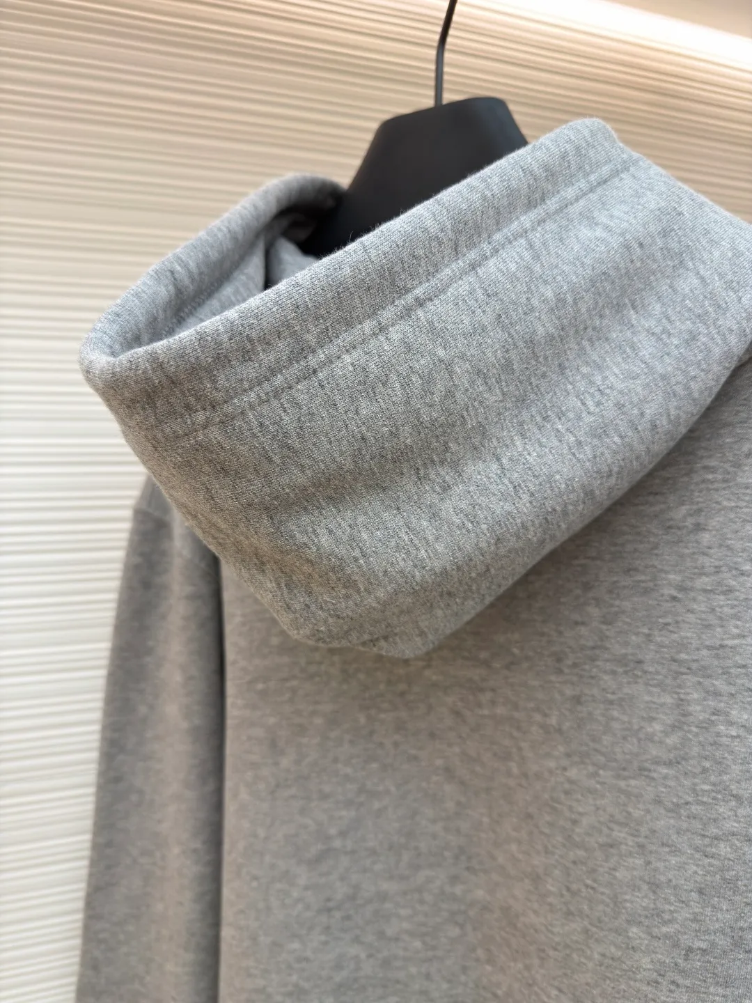 Dior classic logo embroidered hooded sweatshirt ●Item number: 1682332-A75 ●Material: cotton fabric ●Technology: embroidery production ●Color: gray ●Version: fitted version ●Weight: about 645 grams ●Size: XS-S-M-L ●Description: It adopts a fleece fabric structure of 26 counts of double yarn + 10S plush bottom, with a weight of 380g/㎡, and 21 counts of 1x1 ribs with a weight of 470g/㎡. It is used for the cuffs and hem. Its extremely high weight ensures the ultimate thickness, stiffness and deformation resistance of these closing parts, forming a unified and strong outline with the body. The fabric is a heavyweight and high-quality sweatshirt fabric. The 26-count double yarn forms a smooth, delicate and strong outer surface of the fabric, ensuring good color fastness and appearance. The 10S plush base undergoes a precise fleece or brushing process to form a layer of rich, dense and uniform fluff on the inside of the fabric. This makes the sweatshirt have a crisp and skeletal feel on the outside and an extremely soft and warm feel on the inside. White tone twill needle embroidery process. Needle embroidery is a straight line embroidery with stitches closely connected and evenly arranged. It is often used to outline clear and sharp outlines. This stitch is used to embroider a diagonal stripe pattern with a certain angle and width. Use white embroidery thread to follow the preset diagonal trajectory and perform precise embroidery with high-density stitches. On the high-weight fabric base, simple, exquisite and three-dimensional line decoration is created. The contrast between white and fabric color is sharp, and the slightly convex texture brought by the embroidery adds a visual and tactile layer, effectively enhancing the exquisite style of the basic sweatshirt. The overall wiring is straight and delicate, the fabric is comfortable and soft, and the color is consistent without color difference. It can be matched with the same style to create a fashionable look and control various occasions. Customized accessories, complete with three standards, same style for men and women!