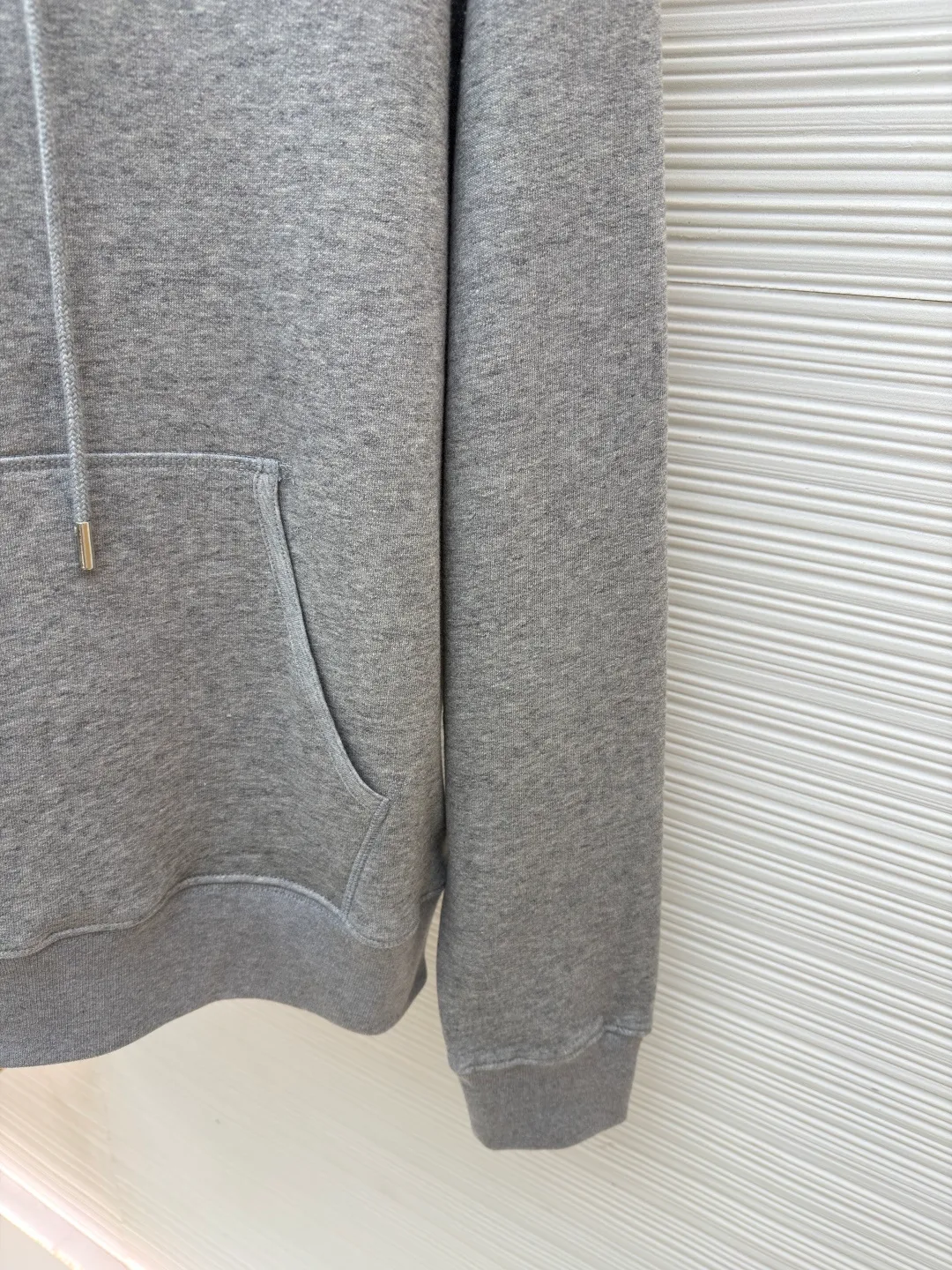 Dior classic logo embroidered hooded sweatshirt ●Item number: 1682332-A75 ●Material: cotton fabric ●Technology: embroidery production ●Color: gray ●Version: fitted version ●Weight: about 645 grams ●Size: XS-S-M-L ●Description: It adopts a fleece fabric structure of 26 counts of double yarn + 10S plush bottom, with a weight of 380g/㎡, and 21 counts of 1x1 ribs with a weight of 470g/㎡. It is used for the cuffs and hem. Its extremely high weight ensures the ultimate thickness, stiffness and deformation resistance of these closing parts, forming a unified and strong outline with the body. The fabric is a heavyweight and high-quality sweatshirt fabric. The 26-count double yarn forms a smooth, delicate and strong outer surface of the fabric, ensuring good color fastness and appearance. The 10S plush base undergoes a precise fleece or brushing process to form a layer of rich, dense and uniform fluff on the inside of the fabric. This makes the sweatshirt have a crisp and skeletal feel on the outside and an extremely soft and warm feel on the inside. White tone twill needle embroidery process. Needle embroidery is a straight line embroidery with stitches closely connected and evenly arranged. It is often used to outline clear and sharp outlines. This stitch is used to embroider a diagonal stripe pattern with a certain angle and width. Use white embroidery thread to follow the preset diagonal trajectory and perform precise embroidery with high-density stitches. On the high-weight fabric base, simple, exquisite and three-dimensional line decoration is created. The contrast between white and fabric color is sharp, and the slightly convex texture brought by the embroidery adds a visual and tactile layer, effectively enhancing the exquisite style of the basic sweatshirt. The overall wiring is straight and delicate, the fabric is comfortable and soft, and the color is consistent without color difference. It can be matched with the same style to create a fashionable look and control various occasions. Customized accessories, complete with three standards, same style for men and women!