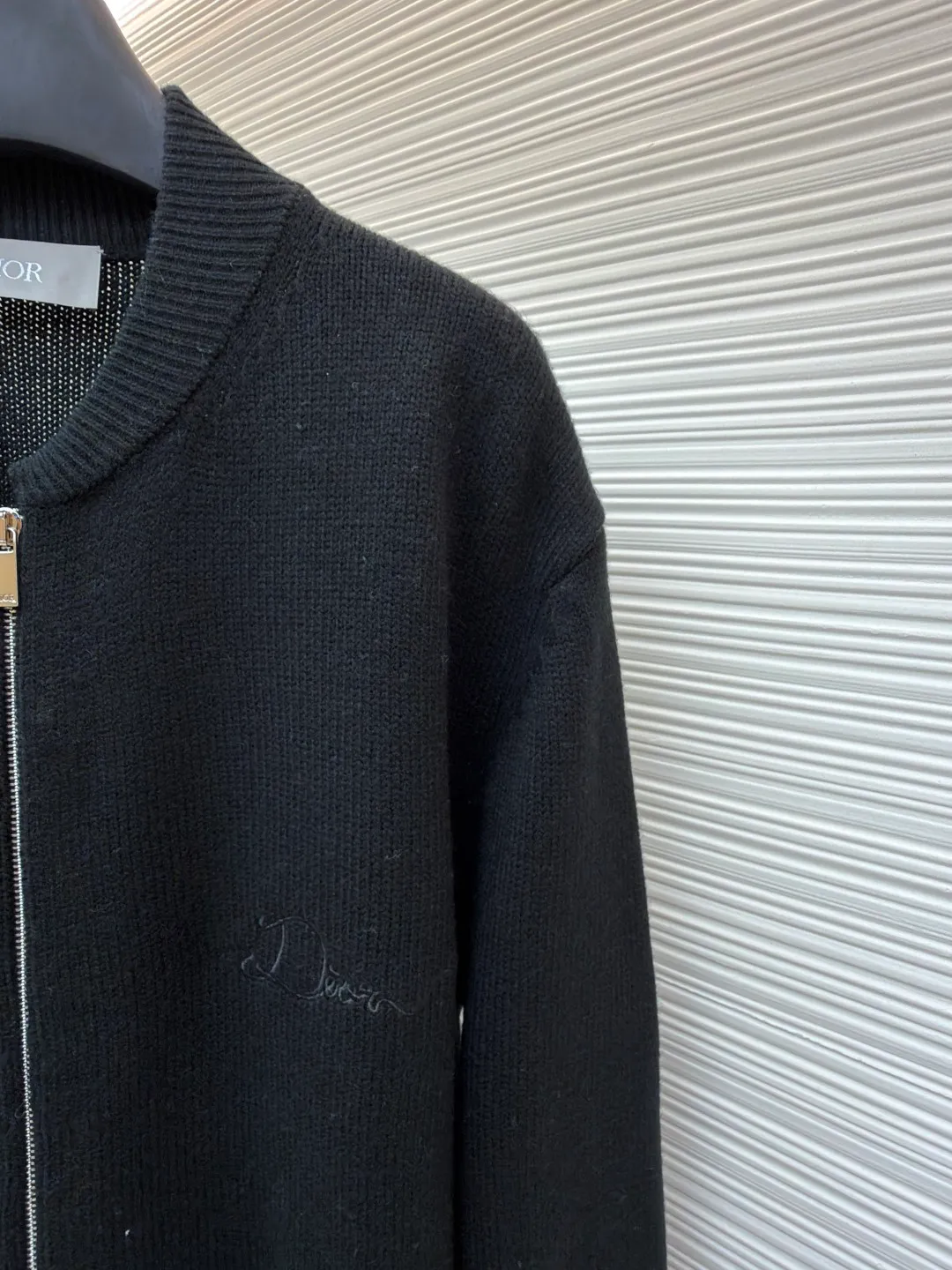 Dior letter embroidered wool knitted cardigan ●Original version: Purchased and developed by 18684 ●Item number: 1682138-C05 ●Fabric: wool blended fabric ●Technology: knitting ●Color: black ●Version: fitted version ●Weight: about 755 grams ●Size: S-M-L-XL ●Description: This Dior black knitted zipper cardigan is made of high-count worsted wool and mulberry silk blended yarn. It is woven with plain knitting technology on an Italian 16-needle computerized flat machine. The yarn is first treated with anti-pilling and pre-shrunk to make the garment soft and resistant to deformation. The Dior logo on the front chest adopts dark embroidery technology, using matte embroidery thread of the same color, completed with 0.1mm fine stitching, which is low-key and rich in texture; the three-dimensional Dior letters on the back use hand-made rope embroidery techniques, and the woven rope straps are fixed segment by section according to the outline of the version, forming a 3D relief effect. The connection between the rope strap and the body adopts invisible locking technology, without any abrupt threads. The inner side of the collar is spliced ​​with breathable mesh fabric, the metal zipper is made of custom matte nickel material, and the teeth are treated with wear-resistant treatment. The ribbed edges of the cuffs and hem have built-in elastic spandex yarn, and are hand-ironed and shaped. Every craftsmanship detail is in line with Dior's high-end ready-to-wear production standards. The overall wiring is straight and delicate, the fabric is comfortable and soft, and the color is consistent without color difference. It can be matched with the same style to create a fashionable look and control various occasions. Customized accessories, complete with three standards, same style for men and women!