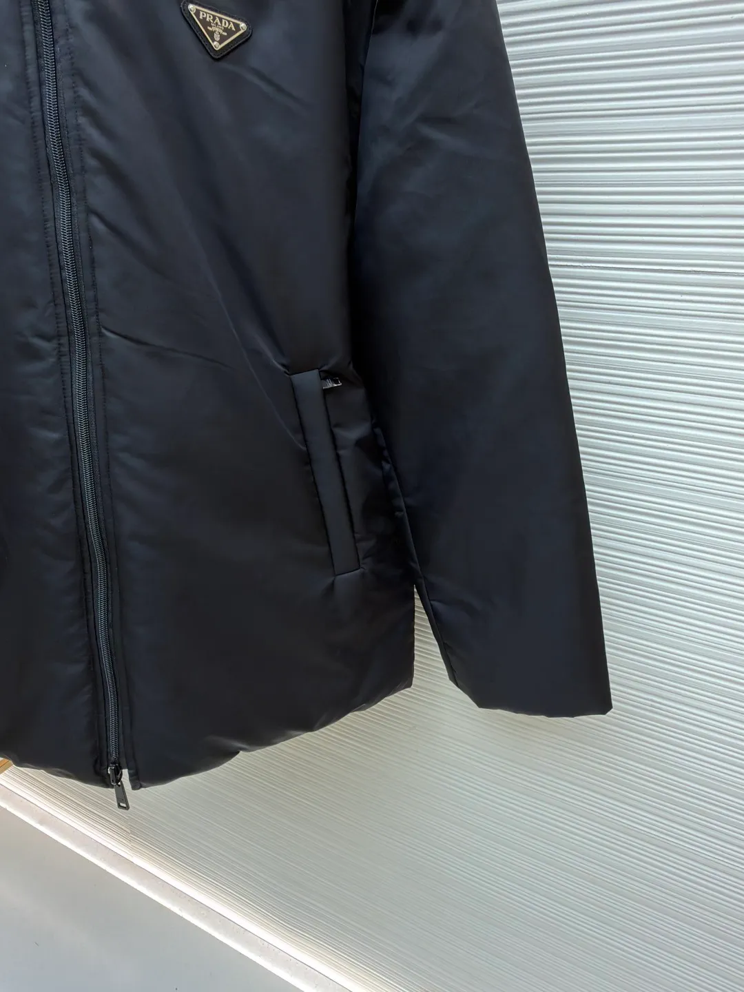 Prada mid-length nylon hooded down jacket ●Original version: purchased and developed for 15999 ●Item number: 1681587-D35 ●Fabric: white duck down fabric ●Technology: mechanical down filling ●Color: black ●Version: fitted version ●Weight: about 1155 grams ●Size: S-M-L-XL ●Description: Re-Nylon short down jacket uses environmentally friendly Re-Nylon material, the fabric density is very high It has strong tear resistance, strong stiffness and wear resistance. It is different from the Bird brand's hard shell, it is softer and has a very strong sense of functionality. Double-sided design: The biggest highlight of this down jacket is its double-sided design, which allows one piece of clothing to show two different styles and shapes, greatly increasing the diversity and fashion sense of wearing. Detachable hood: The down jacket is equipped with a detachable nylon hood, which users can easily remove or install according to weather changes or personal preferences, which is both practical and convenient. The details are exquisitely processed: the zipper design is simple and elegant, easy to operate; the closing design of the cuffs and hem effectively prevents the intrusion of cold wind, improving the warmth and comfort of wearing. All the hangtags, wash marks, air holes, snap buttons, and chest labels are all custom-made using original one-to-one molds.  The overall wiring is straight and delicate, the fabric is comfortable and soft, and the color is consistent without color difference. It can be matched with the same style to create a fashionable look and control various occasions. Customized accessories, complete with three standards, same style for men and women!