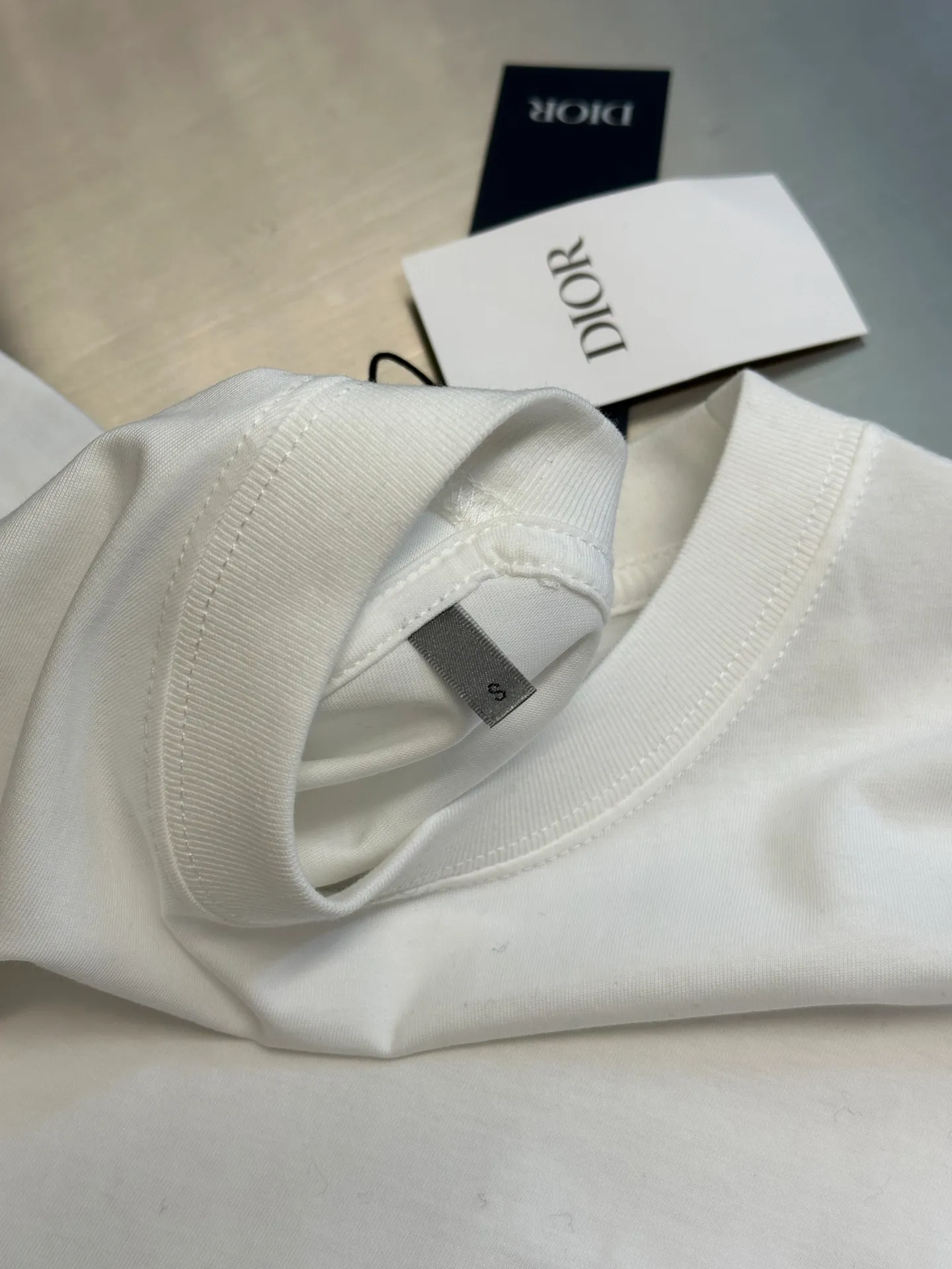 🅿️260 Dior Love Series Pocket Embroidery Round Neck Short Sleeve Cotton Jersey Fabric. Made of 24S special woven compact cotton fabric, 185g; with 32S double yarn thread, 300g. The strength of compact yarn is higher than that of traditional single yarn. The single fibers in compact yarn are closely arranged, which helps to improve the strength of the yarn. The ends of the fibers are all twisted into the yarn, so the yarn is very tight and the yarn has a smooth appearance with less hairiness. Compact spinning yarn has higher strength and less hairiness, making it less prone to fraying.  The chest is decorated with embroidery patterns, and the main body adopts precision stitch embroidery technology; the embroidery is very fine and dense, with clear patterns and strong lines and three-dimensionality. The linen material embroidery thread is combined with encrypted processing, and the embroidery body has a subtle matte visual texture; the embroidery effect is three-dimensional and full. The flat embroidery has a unique needle-to-needle design, and the embroidery is very fine and dense. The overall stitching is fine, with consistent fineness and texture, adding a sense of layering to the simple design.  Standard crew neck, short sleeve fit. The neckline is rounded and arc-shaped, suitable for various face shapes and body shapes; the sleeve length is moderate and ends just above the elbow, showing a smart and neat image. The slim fit can show off the wearer's body curves without sacrificing comfort. The collar, cuffs, hem and other parts are all sewn with fine double-needle stitching.  size：xs s m l