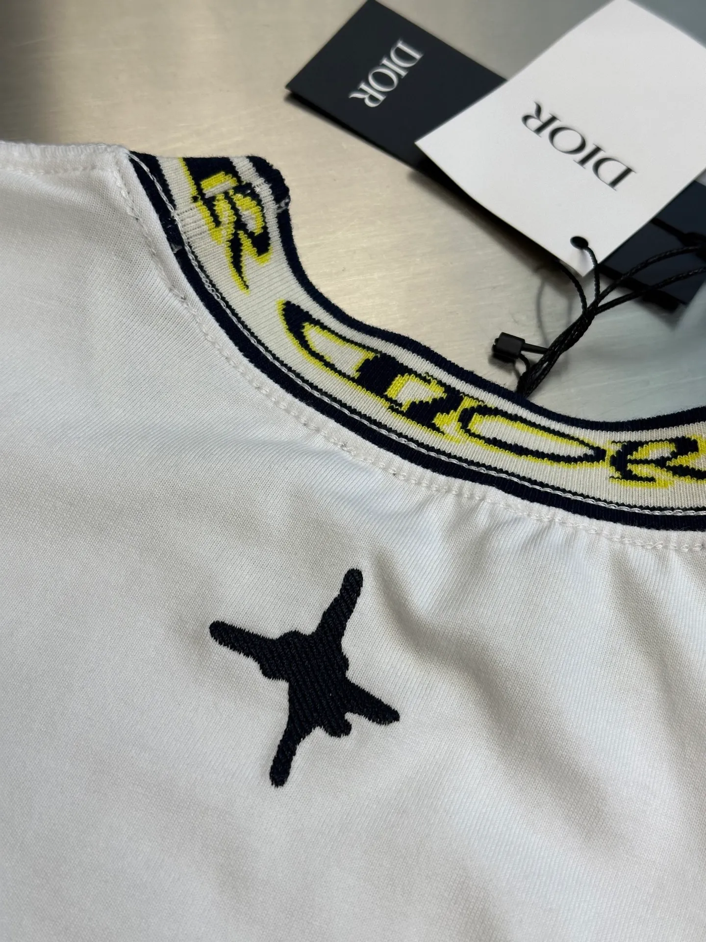 🅿️270 Dior artistic font rib short sleeves, cotton jersey fabric, made of 15S fine cotton plain weave, 230g; with threaded 32S double yarn rack, 300g. 15S is a relatively thick yarn used to make thicker and more durable fabrics. The fabric made of pure cotton natural fiber has the characteristics of good hygroscopicity, strong breathability, softness and comfort. Cotton fabrics are generally suitable for summer wear and can help keep your body dry and comfortable. The yarn passes alternately in the horizontal and vertical directions to form a simple cross structure; it has good elasticity and wear resistance.  The ribbed neckline is decorated with the joint series logo, the original artistic font is painted with flowers, and the flower collar pattern is woven with specific yarns of different colors. Fully computerized jacquard machine, the so-called computerized jacquard machine is to store the pattern data in a computer disk in advance, then put the disk into the computer of the loom, and the computer will control the weaving. The exquisite jacquard flat machine collar has clear and unique texture, rich color layers and is not easy to deform. Special double-layer weaving technology, rich color layering, strong three-dimensional jacquard effect on the surface, comfortable and skin-friendly, and good breathability.  The high-neck flat knit short-sleeved version and the round-neck short-sleeved T-shirt are restored in the design of the collar and cuffs, and special sewing methods or reinforcements are used to ensure the durability and comfort of these parts. Standard casual round neck short sleeves usually adopt a classic round neck design. The neckline is moderate in size, neither too tight nor too loose, and can well show the wearer's neck line.  size：xs s m l