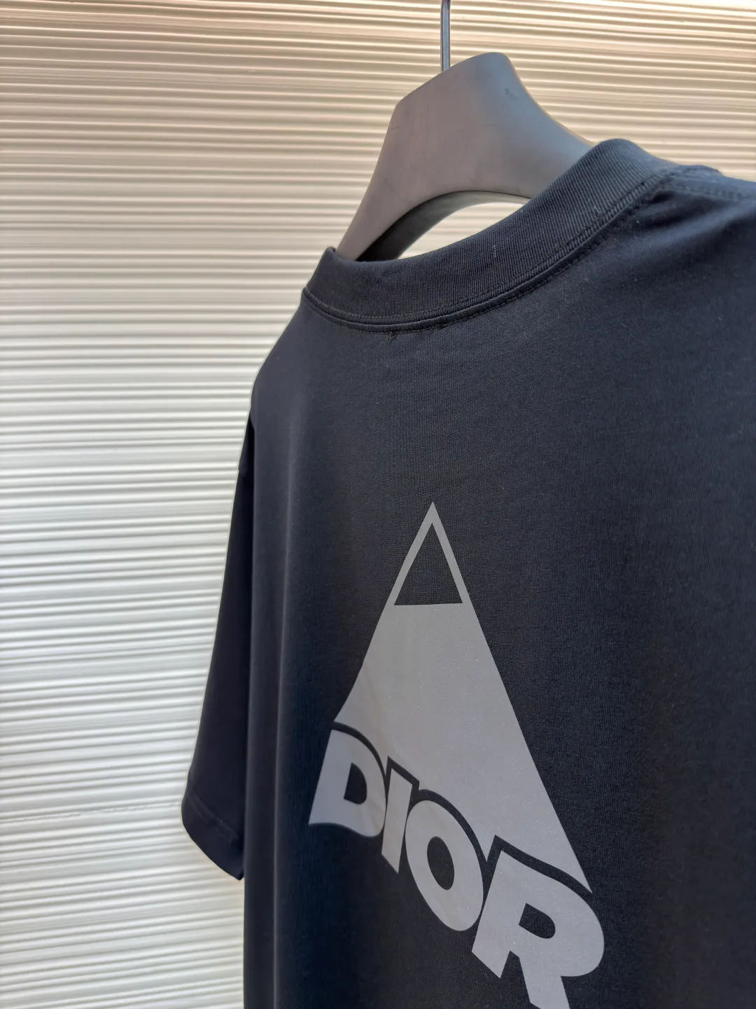 Dior Reflective Triangle Icon Round Neck Short Sleeve ●Original version: Purchased and developed by 6323 ●Item No.: 1681099-A00 ●Fabric: Jersey fabric ●Technology: Reflective lettering and embossed production ●Version: Fitted version ●Weight: about 220 grams ●Size: S-M-L-XL ●Description: The main body is made of 24S special woven compact cotton to make jersey fabric, weight 180g. High-count combed cotton yarn eliminates most of the short hairiness through compact spinning process, making the yarn smoother and stronger. The woven fabric structure is extremely dense, flat and soft, with excellent anti-pilling ability and durability, while retaining the natural advantages of pure cotton, which is breathable and skin-friendly. The neckline is made of 32S 1x1 rib with a weight of 300g. The finer yarn count creates a more delicate and tight thread, which provides better elasticity and deformation resistance than ordinary ribs, ensuring that the neckline can still remain stiff after being put on and taken off many times. The reflective engraving and embossing process is a sophisticated technology that combines safety functions with visual aesthetics. The core is to use a reflective lettering film with a built-in micro-glass bead layer. First, a high-precision laser cutting machine is used to engrave the outline according to the designed fonts and patterns to ensure that the edges are clear and burr-free. The cut reflective film is accurately attached to the surface of the fabric through heat transfer printing equipment under specific temperature and pressure, so that it is firmly combined with the fabric fibers. The case is matte silver-gray under normal conditions, but when illuminated by light, the micro-glass bead layer can achieve efficient retroreflection and instantly present a striking bright effect. The finished product is washable and abrasion resistant, perfectly meeting the dual needs of sportswear for functionality and visual tension. The overall wiring is straight and delicate, the fabric is comfortable and soft, and the color is consistent without color difference. It can be matched with the same style to create a fashionable look and control various occasions. Customized accessories, complete with three standards, same style for men and women!