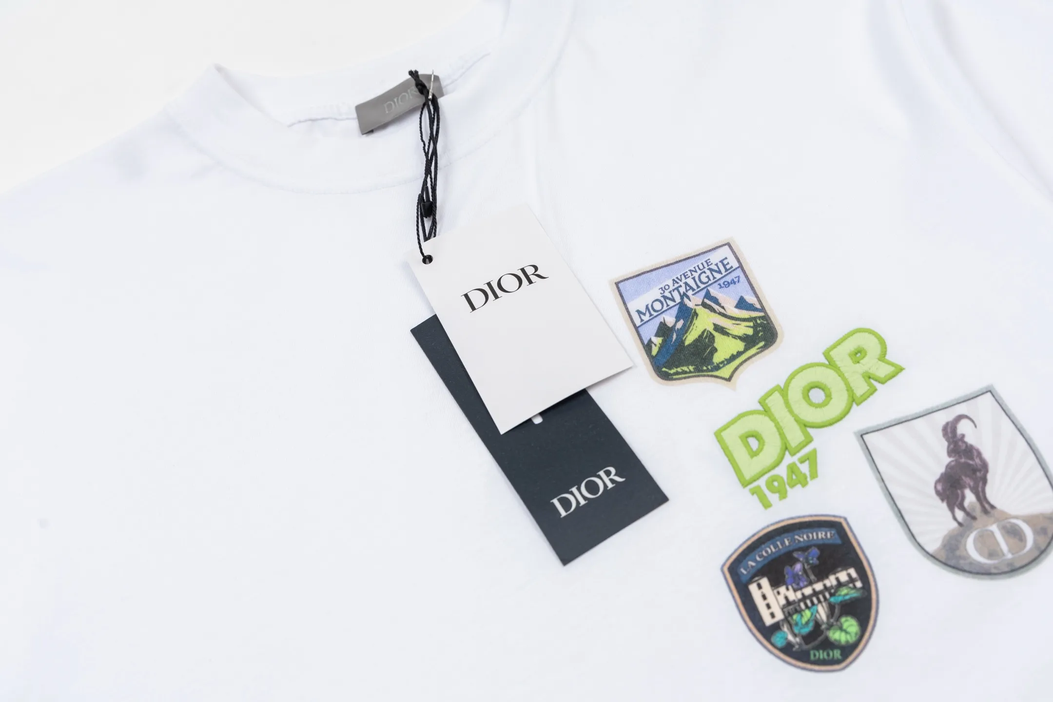 🅿️280 CD Mountain Alpine Shield Printed Short Sleeve (White) The fabric is made of 24S 185g special woven compact cotton fabric, and the rib is made of 32S 300g double yarn rib. This Mountain T-shirt is a new product of the 2026 spring men's wear series. It is decorated with multi-color patches to show the mountain spirit and the classic logo of high-end style inspired by archives. Crafted from white cotton jersey, it features a crew neck for a refined look. The fabric is made of 24S special-spun compact cotton as a plain knitted base. The high-count compact spinning process ensures that the fabric has an extremely delicate skin feel and excellent anti-pilling durability. The neckline is equipped with 32S 1x1 high-density ribbing, which provides long-lasting rebound with its tight structure and protects the collar shape. The decorative multi-color embroidery patch adopts appliqué technique. Three-dimensional lines and fluorescent details are first embroidered with high-density stitches on independent fabrics, and then accurately covered on the chest, forming a strong visual hierarchy and tactile contrast. The alpine element pattern uses digital white ink direct injection technology, with saturated colors and sharp edges, which together with the embroidery patch create a rich texture. Size:XS-S-M-L